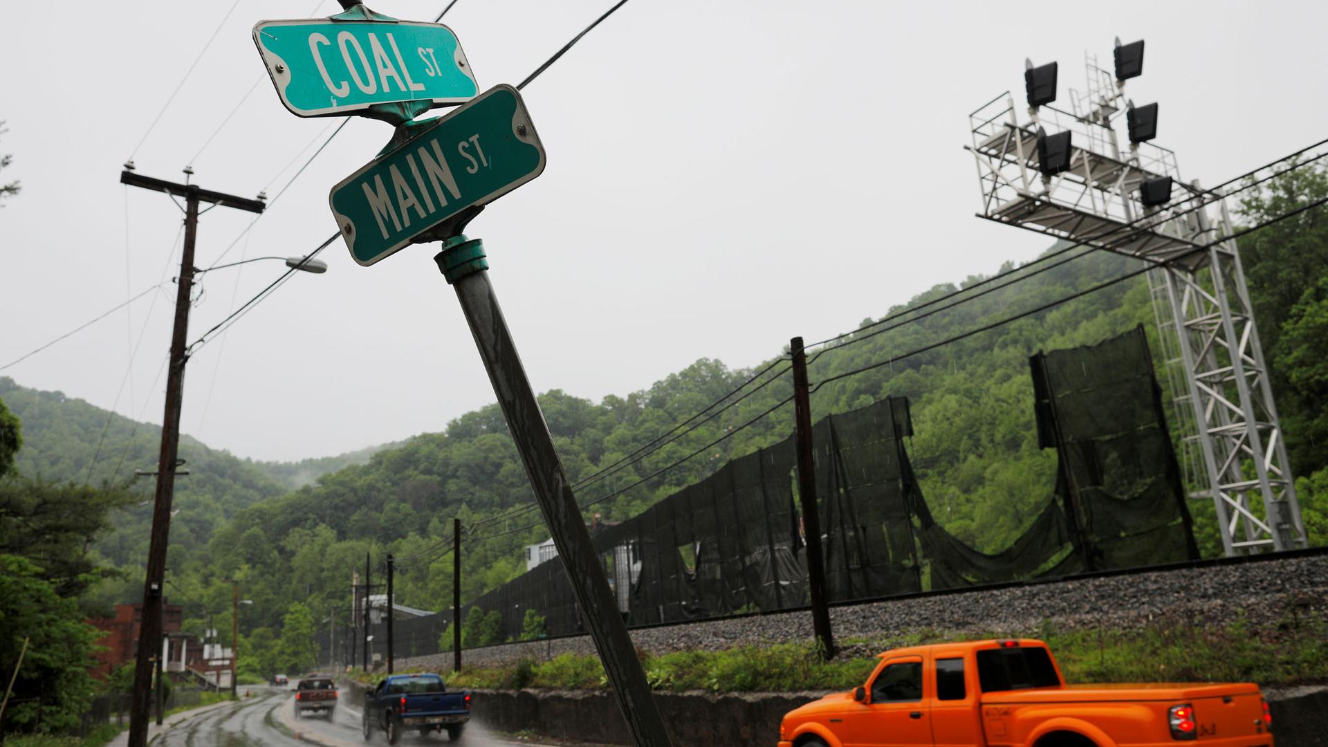 Three pick-up trucks drive down a wet road passing a street sign indicating the intersection of Coal Street and Main Street in Keystone, West Virginia, 2018.