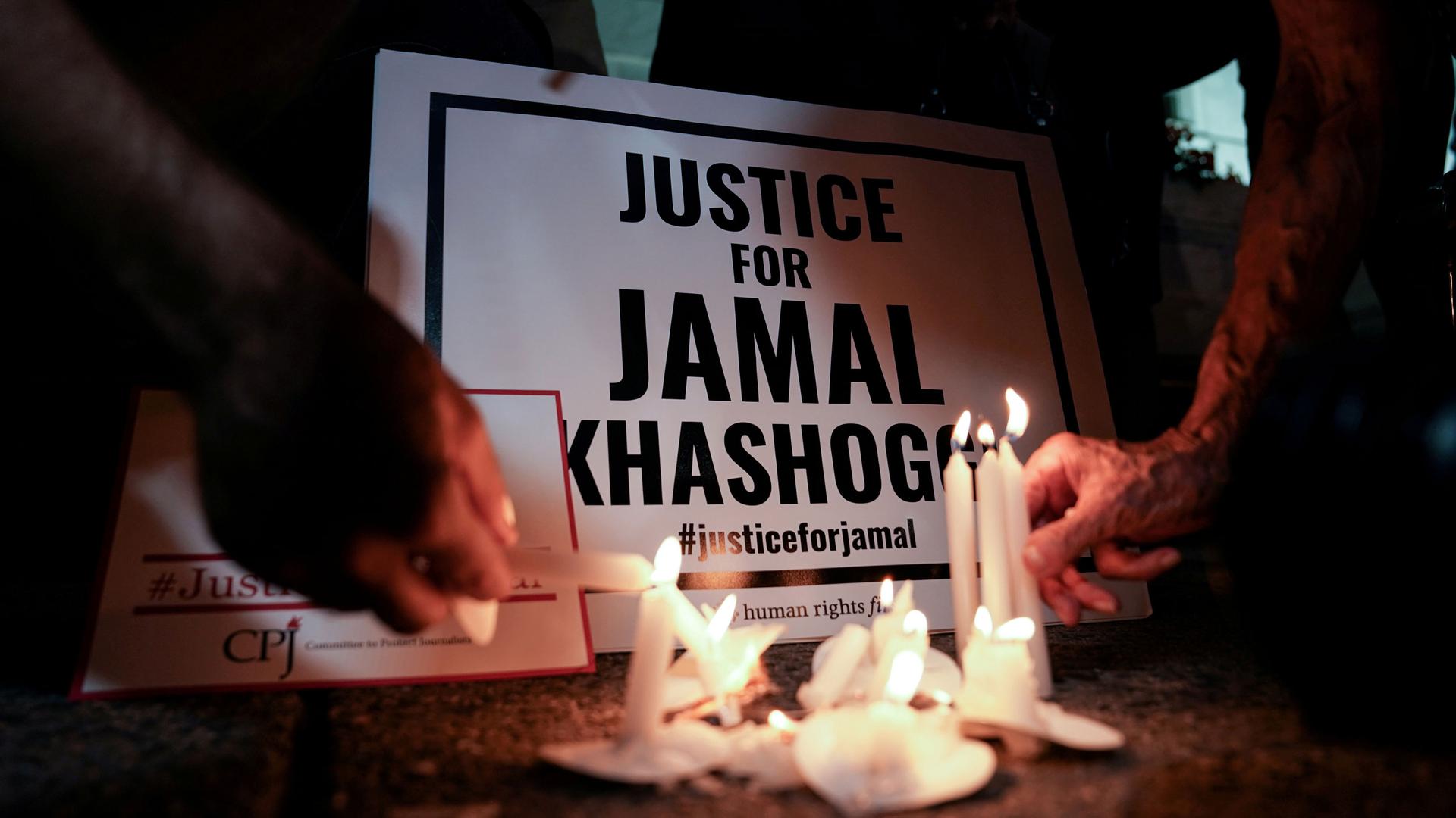 Several white candles are burning in front of a sign that reads, "Justice for Jamal Khashoggi."