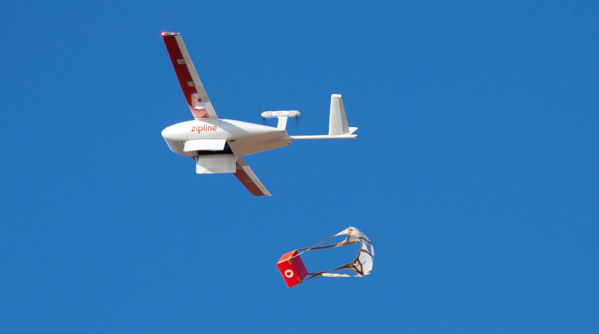 A small drone drops a red package
