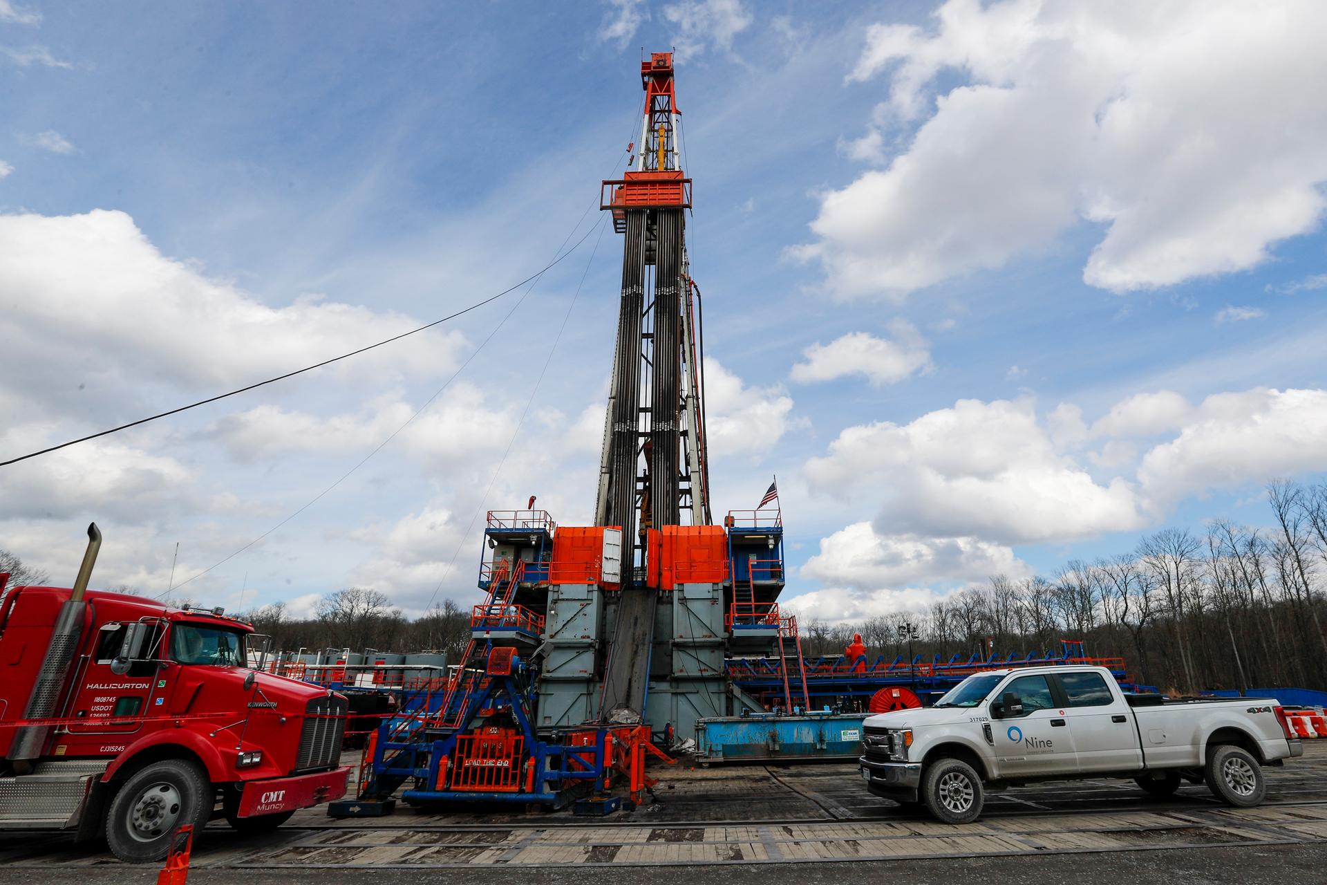 Red and white trucks flank a tall drilling well pictured against the sky