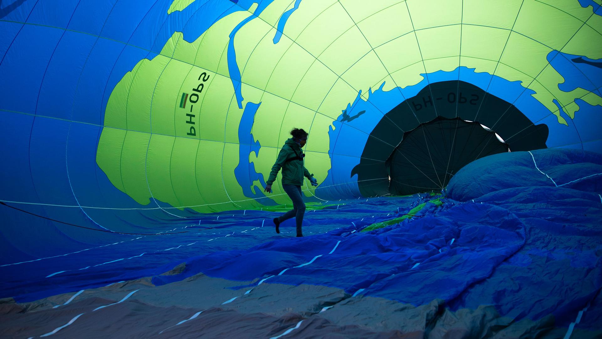 A person is shown in shadow walking on the fabric of a blue and green hot air balloon.