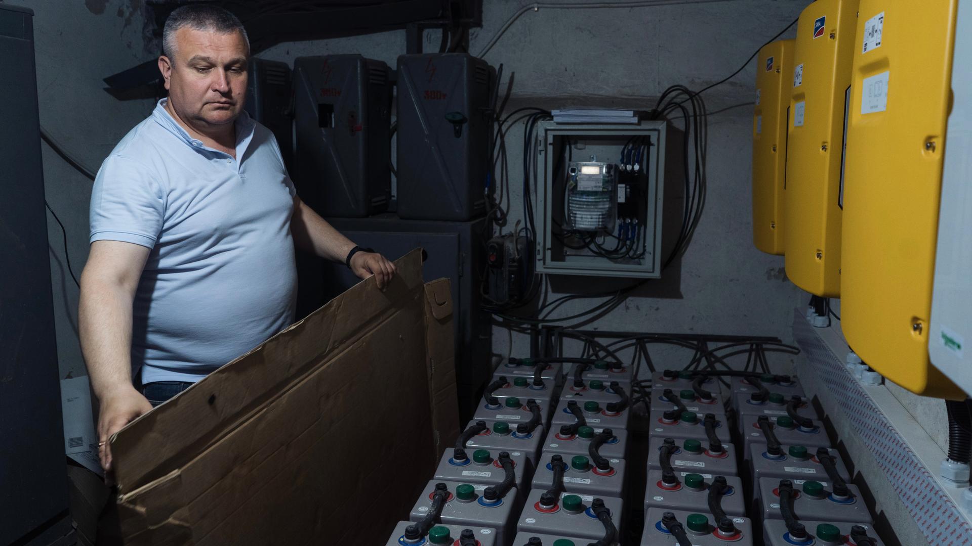 A man standing in a dimly lit room showing large renewable batteries