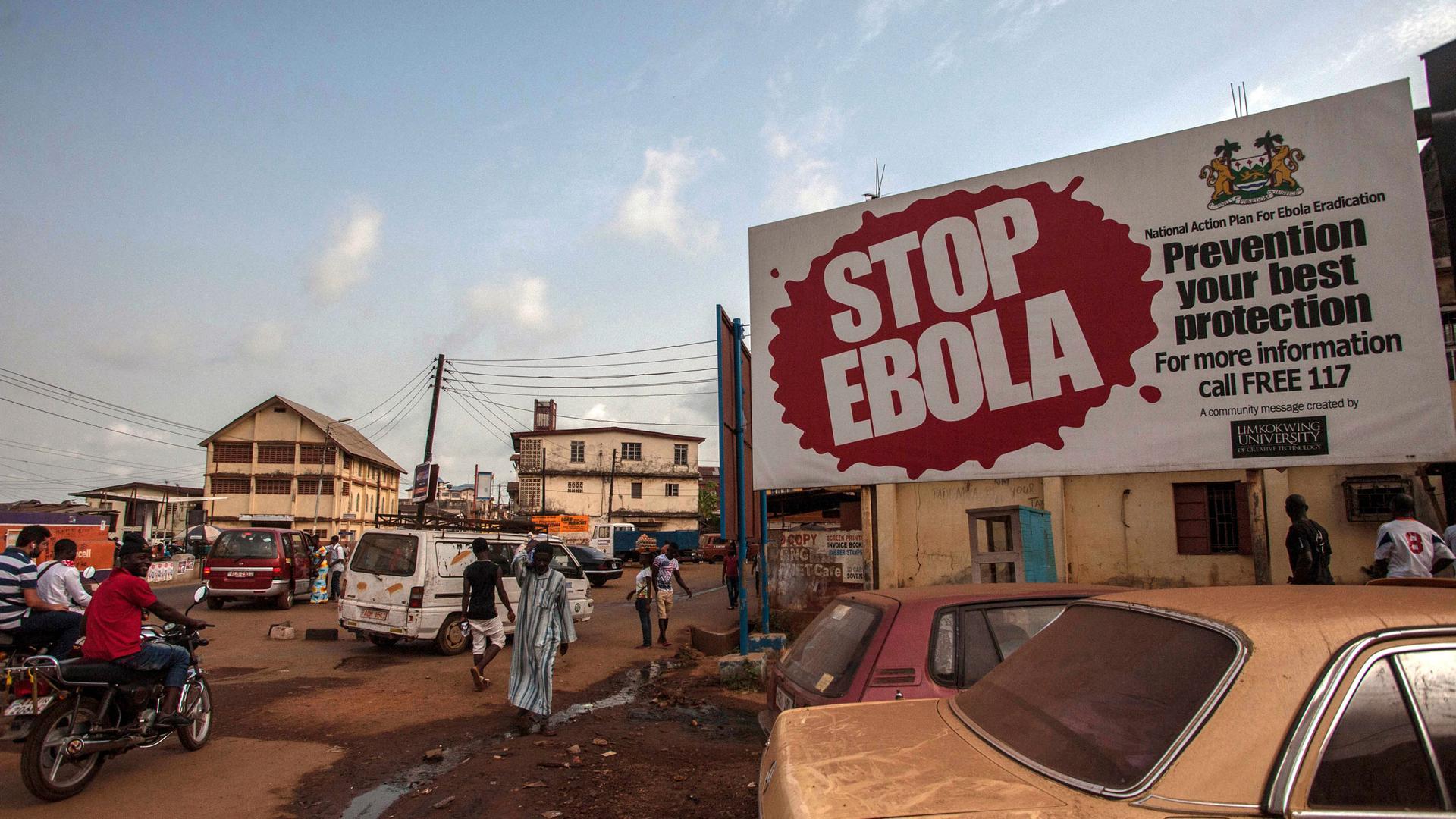 In this Friday, Jan. 15, 2016, file photo, people pass a banner reading "STOP EBOLA," forming part of Sierra Leone's Ebola free campaign in the city of Freetown, Sierra Leone. 