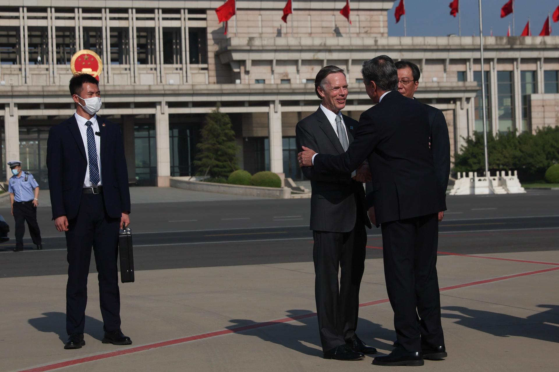 three diplomats shake hands in front of an embassy building