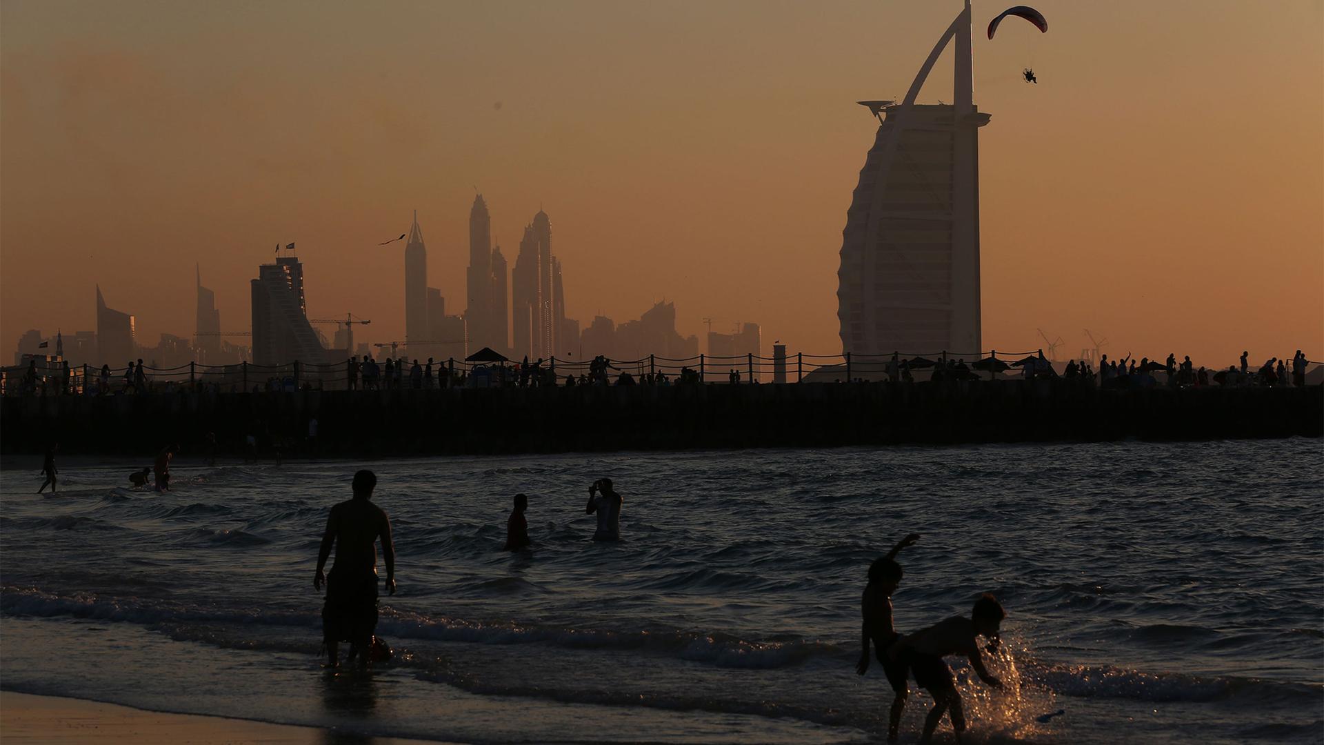 Children play in the surf at Kite Beach with the Burj al Arab, the Dubai Marina and a man flying a powered parachute in the background in Dubai, United Arab Emirates, Jan. 8, 2016.