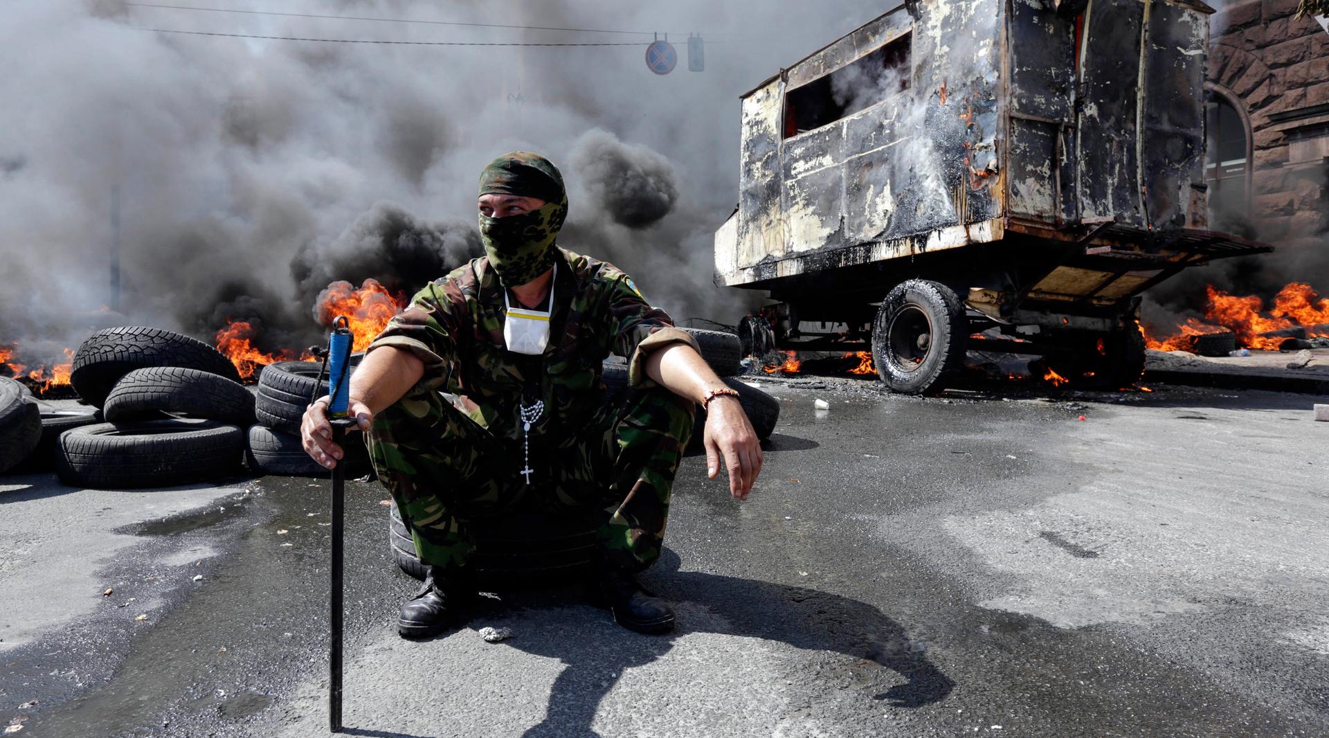 A protester sits in front of burning barricades during clashes with pro-government forces at Independence Square in Kiev, Ukraine on Aug. 7, 2014.