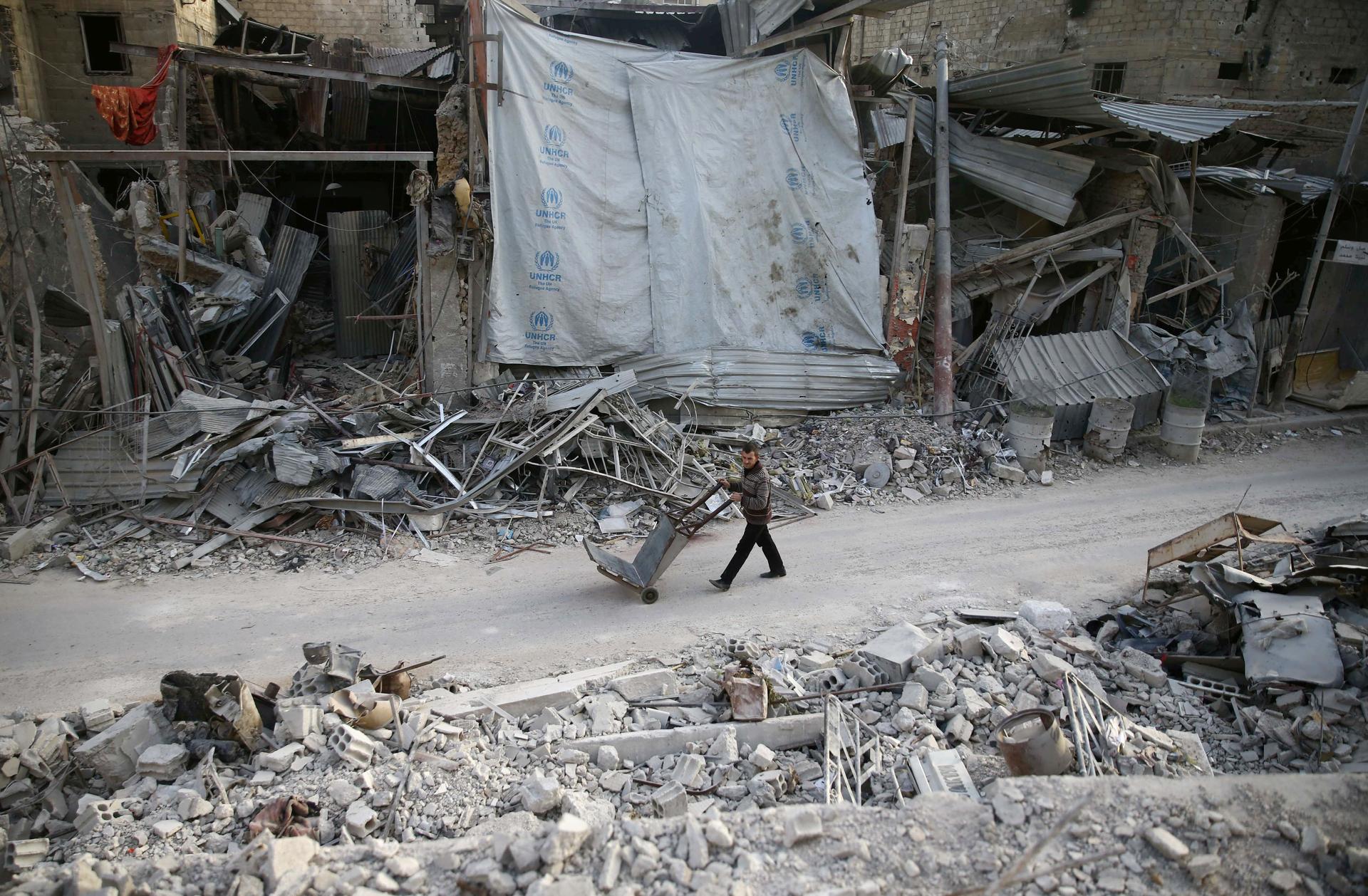 A man pushes a cart past several destroyed buildings in Eastern Ghouta, Syria.