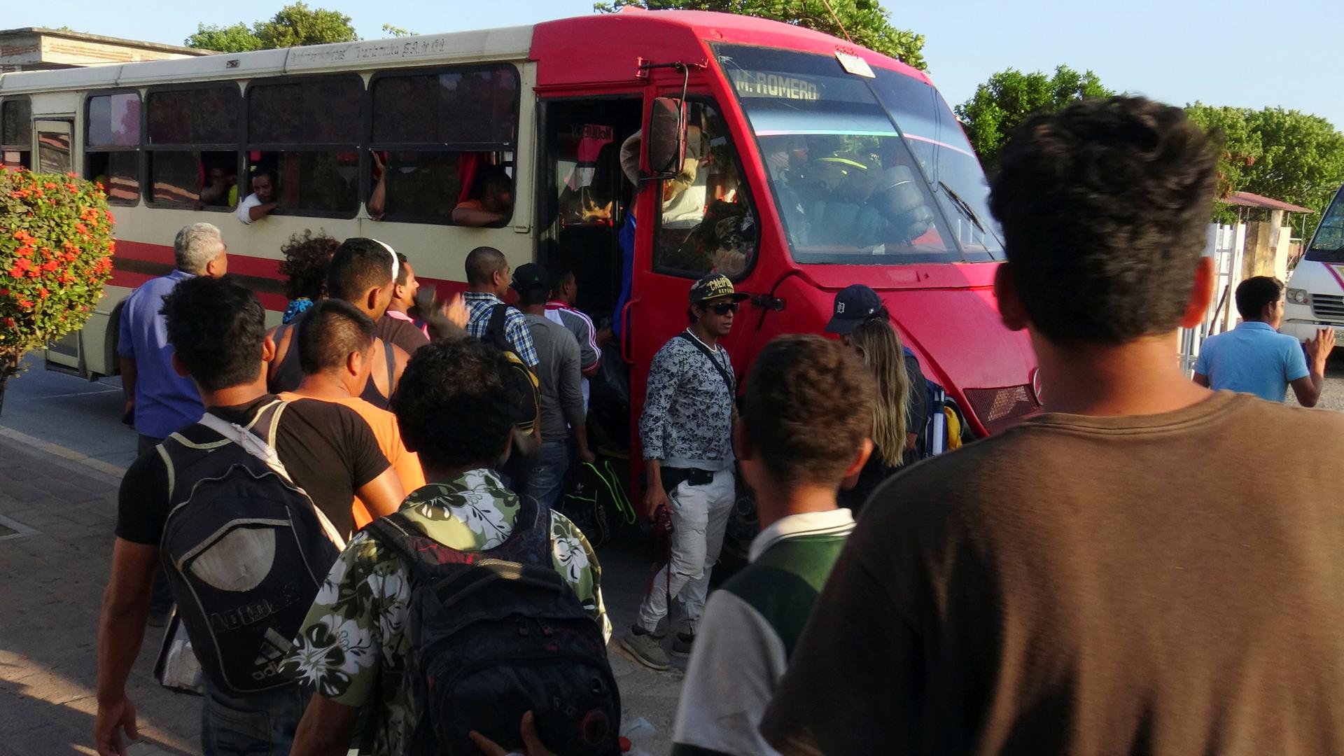 Migrants board a red and white medium size bus in Oaxaca.