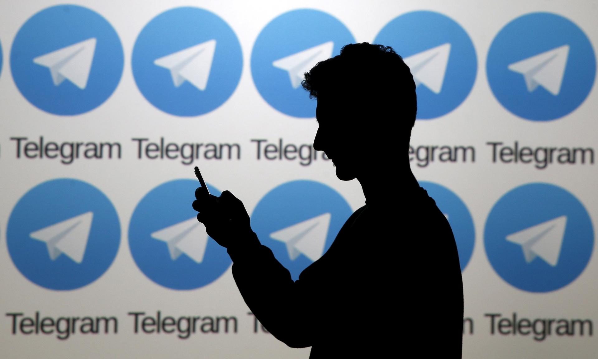 Two men pose with smartphones in front of a screen showing the Telegram logo.