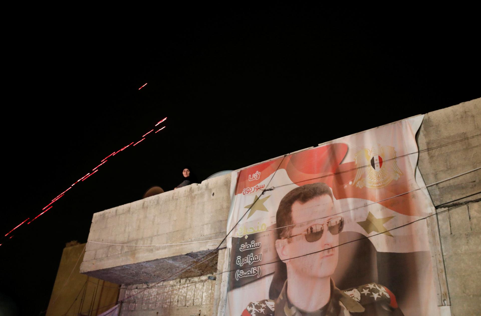 A poster of Syrian President Bashar al-Assad is seen as a woman watches while buses carrying freed hostages and rebels who were evacuated from the rebel-held city of Duma arrive at Wafideen camp in Damascus, Syria April 8, 2018.