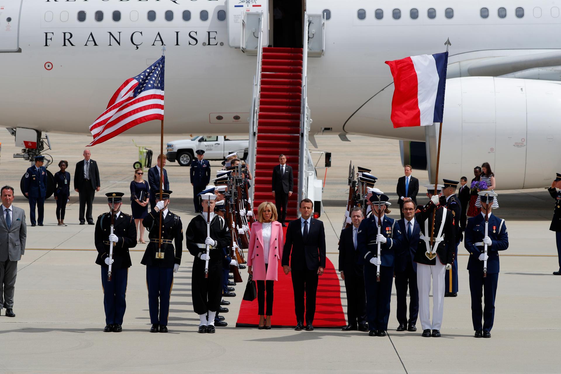 French President Emmanuel Macron and his wife Brigitte Macron stand at the end of a red carpet after deplaning in Maryland with the US and French flags in the background.