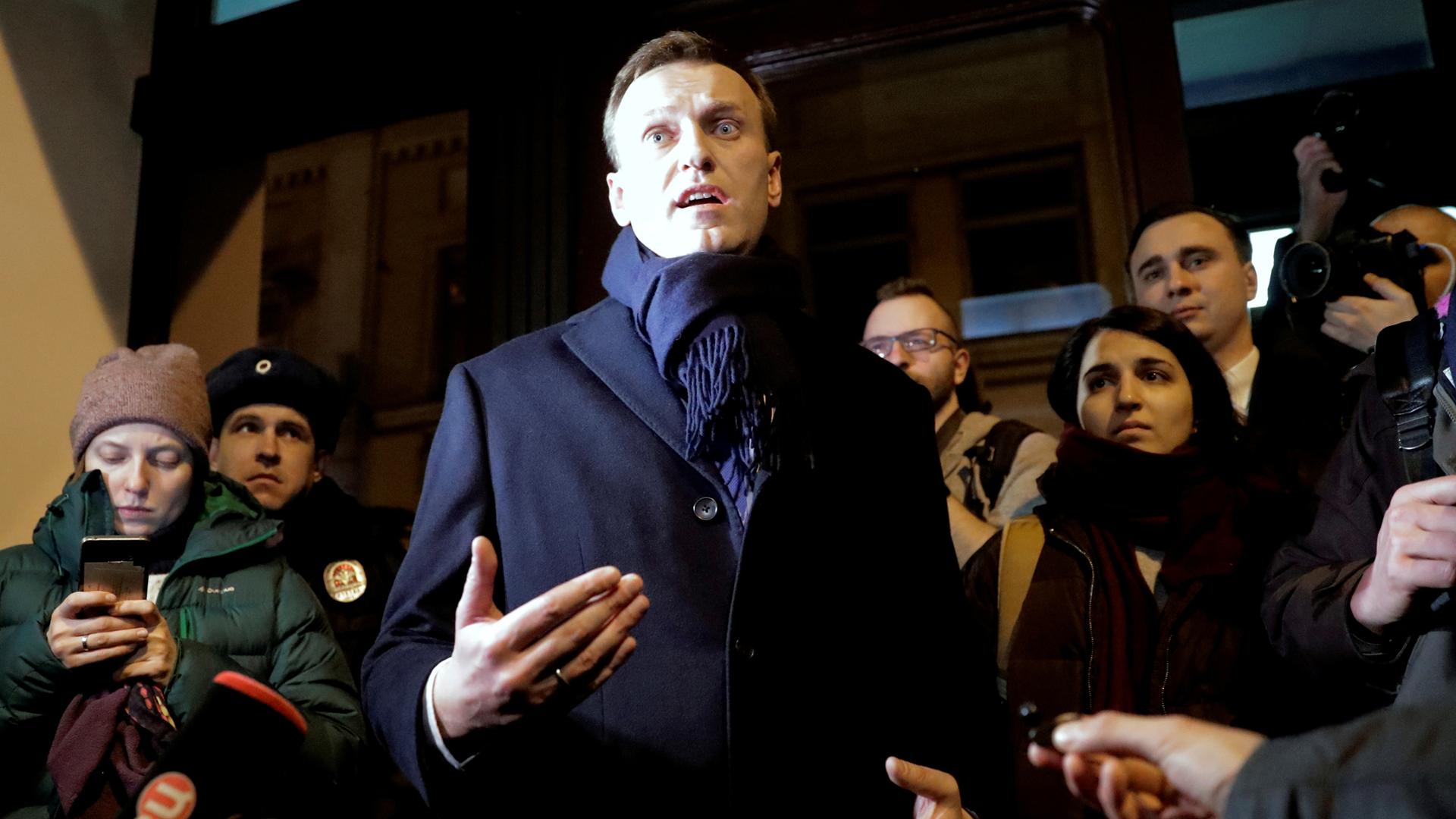 Russian opposition leader Alexei Navalny, wearing a dark overcoat and scarf, addresses the media.