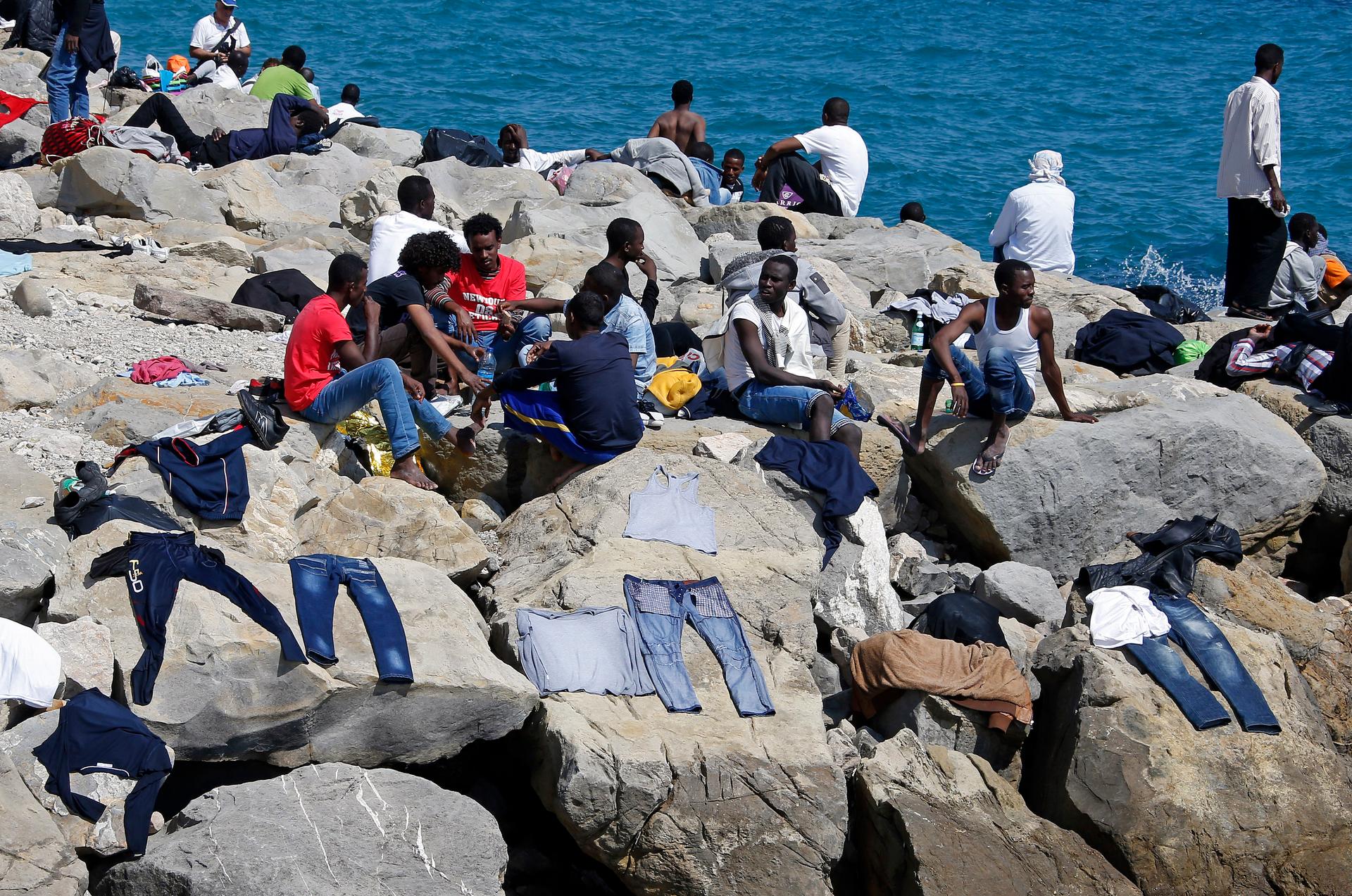 A group of migrants sit near their clothes that dry on the seawall at the Saint Ludovic border crossing on the Mediterranean Sea between Vintimille, Italy and Menton, France, June 14, 2015.