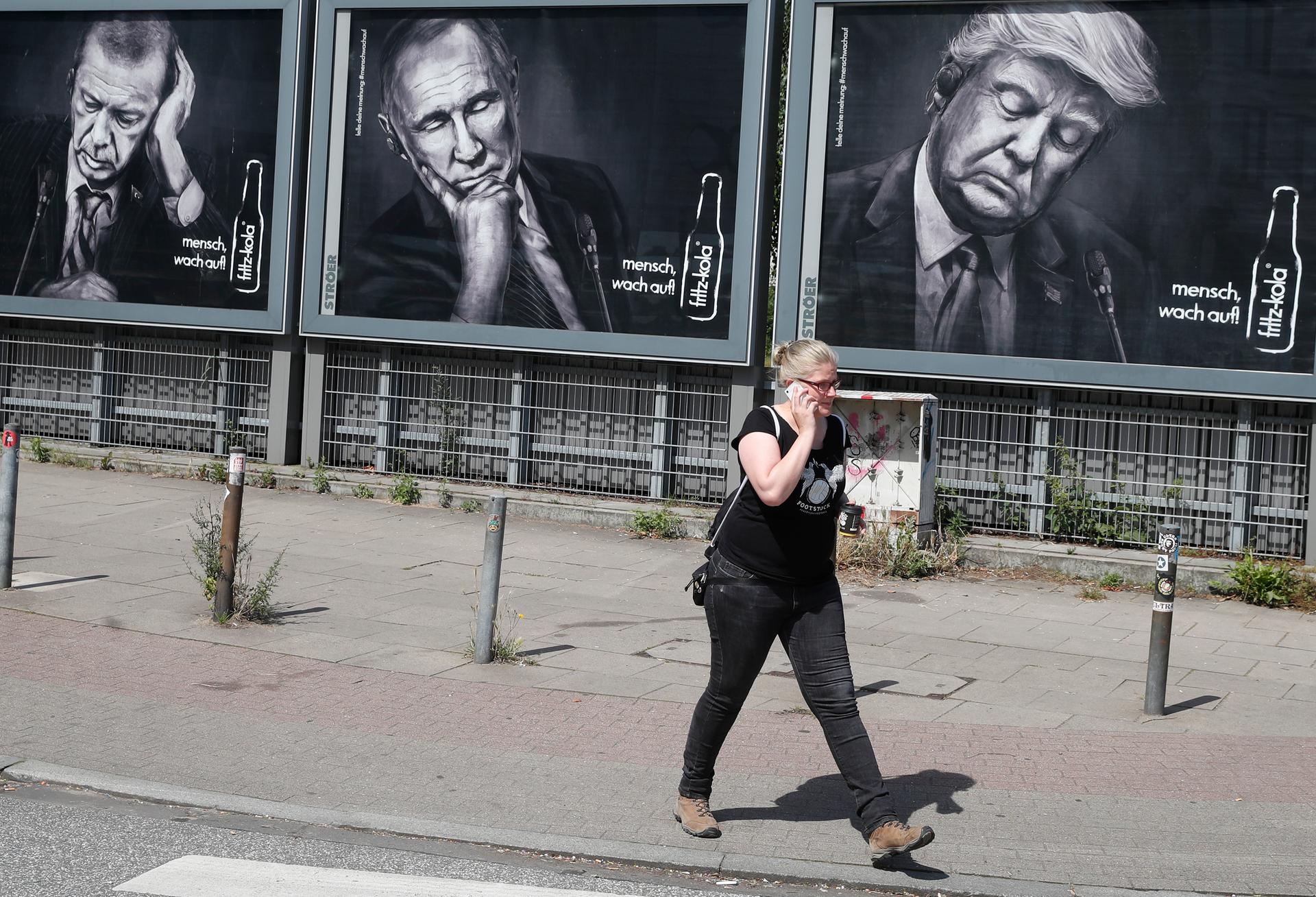 A woman walks past advertising posters of a German soft drink producer depicting Turkey's President Tayyip Erdogan, Russian President Vladimir Putin and President Donald Trump.
