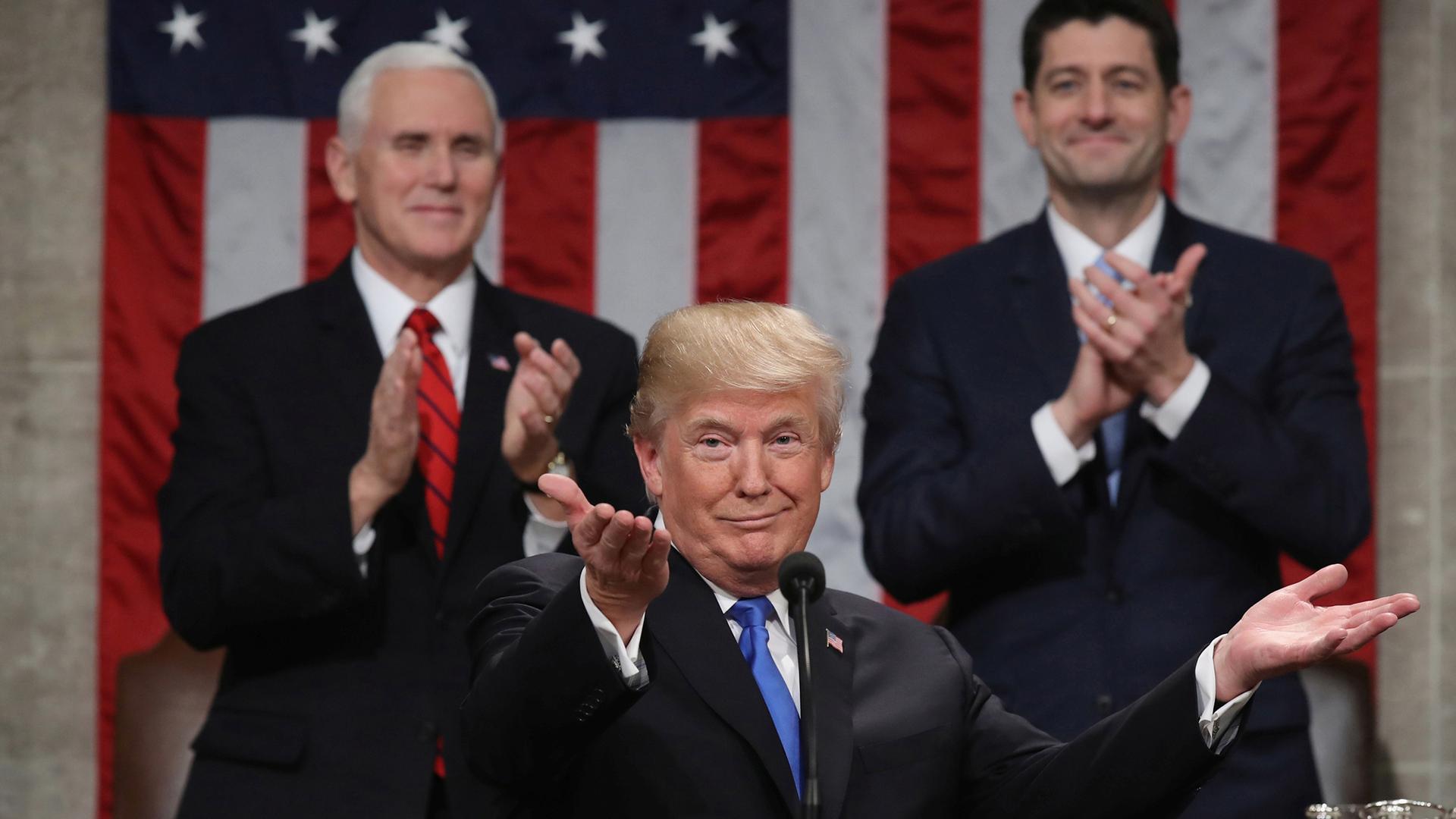 President Donald Trump stands at a podium, center, with Vice President Mike Pence and Speaker of the House Paul Ryan behind him.