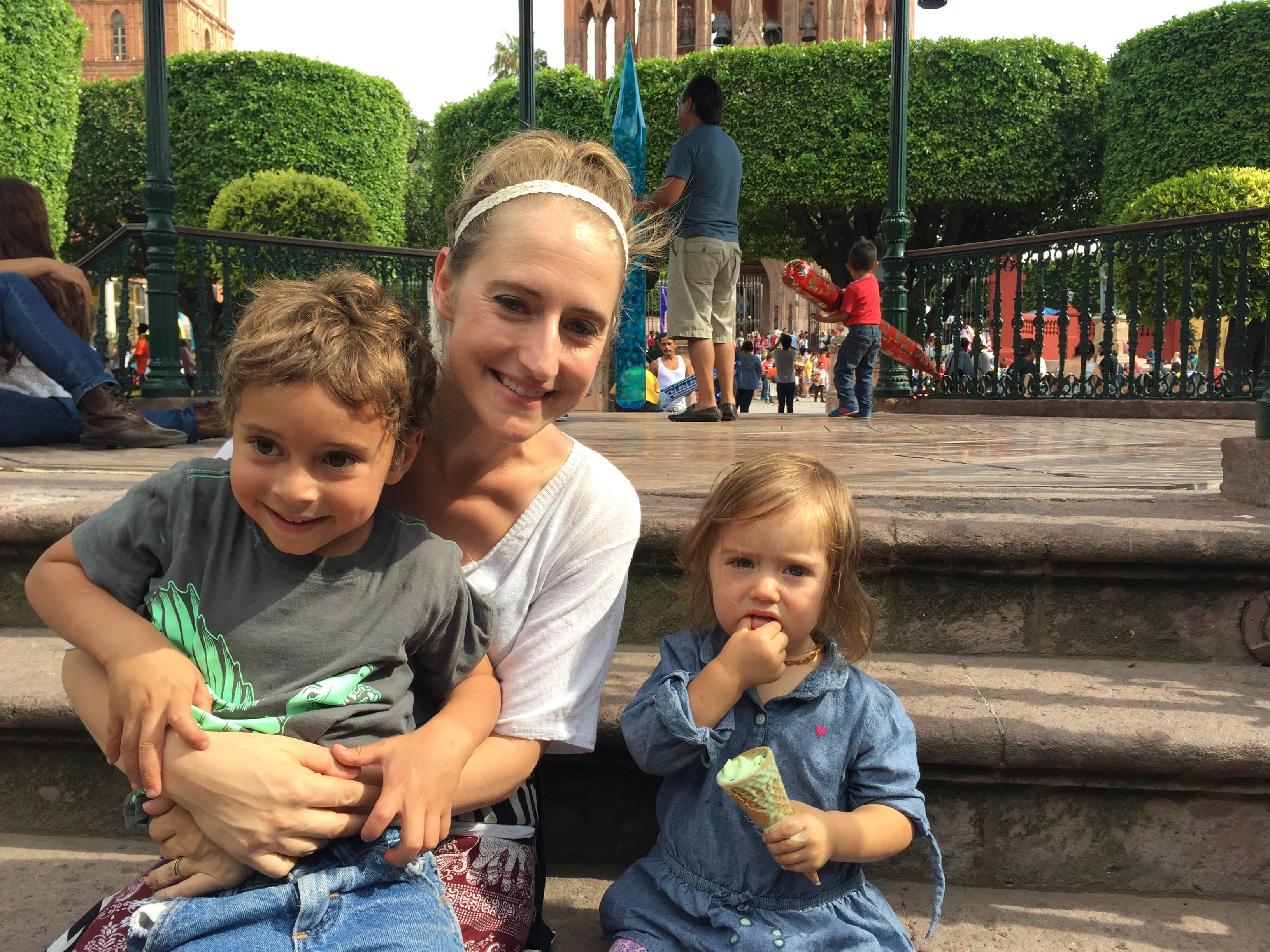 Woman sitting on steps in plaza with two small children. Younger child, a girl, is eating ice cream.