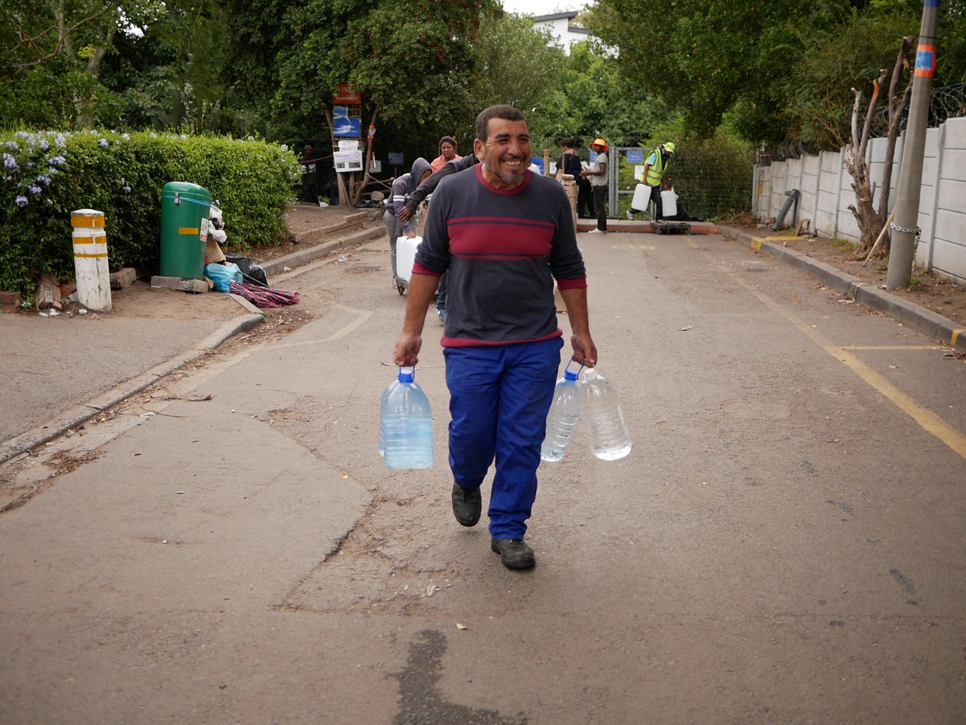 In each hand, Abbas Mustafa carries one of the 18 bottles of water he filled at a spring in Newlands, Cape Town.