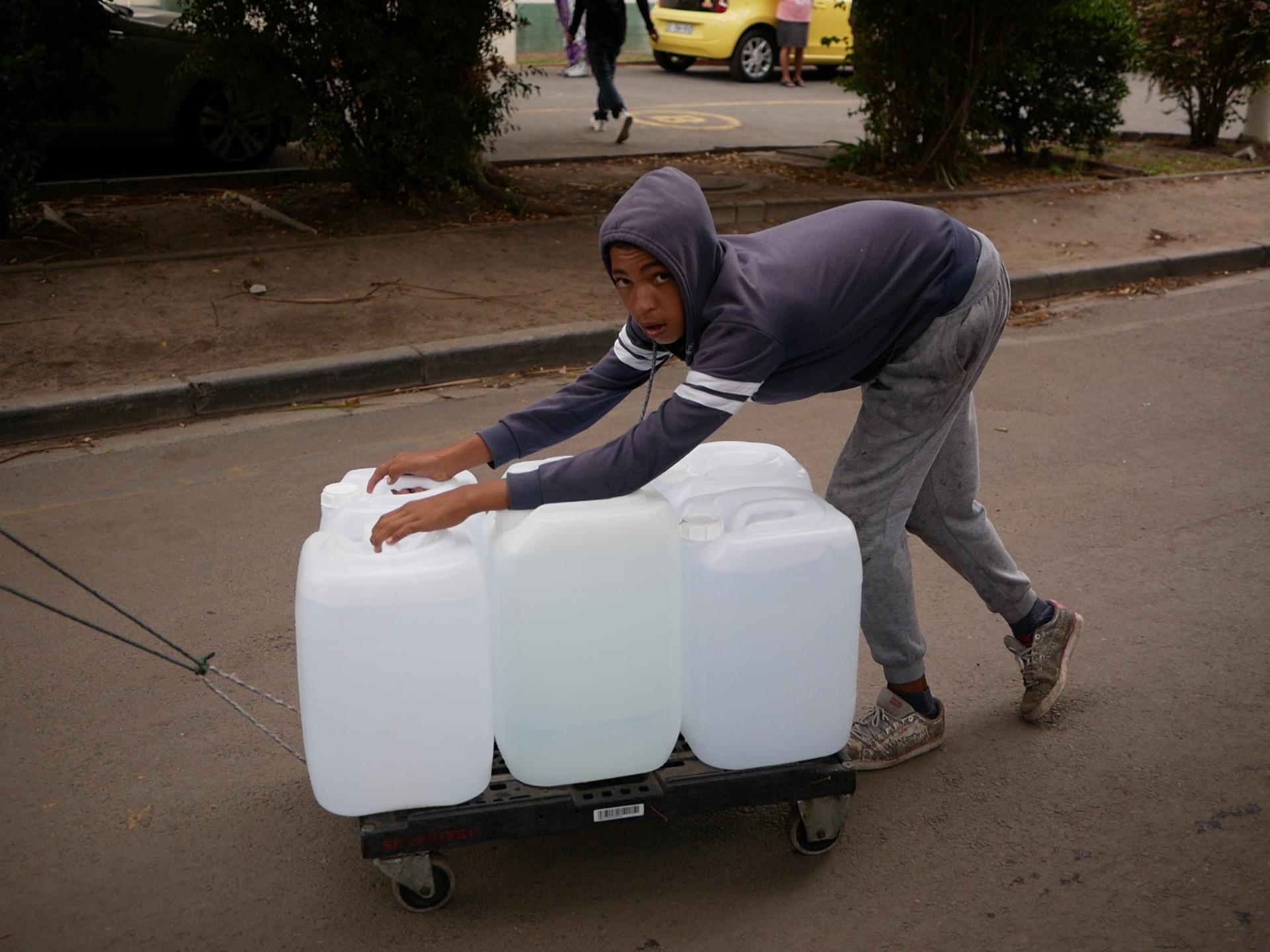 A boy pushes a trolley bulging with white water bottles uphill from the spring.