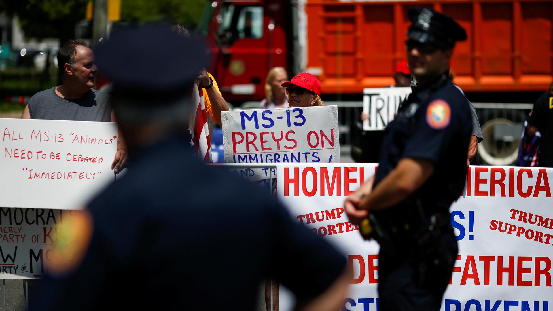 Police stand along barricades while protesters hold signs about the MS-13 gang.