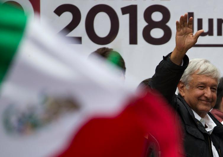Andrés Manuel López Obrador waves to a crowd in front of Mexican flag