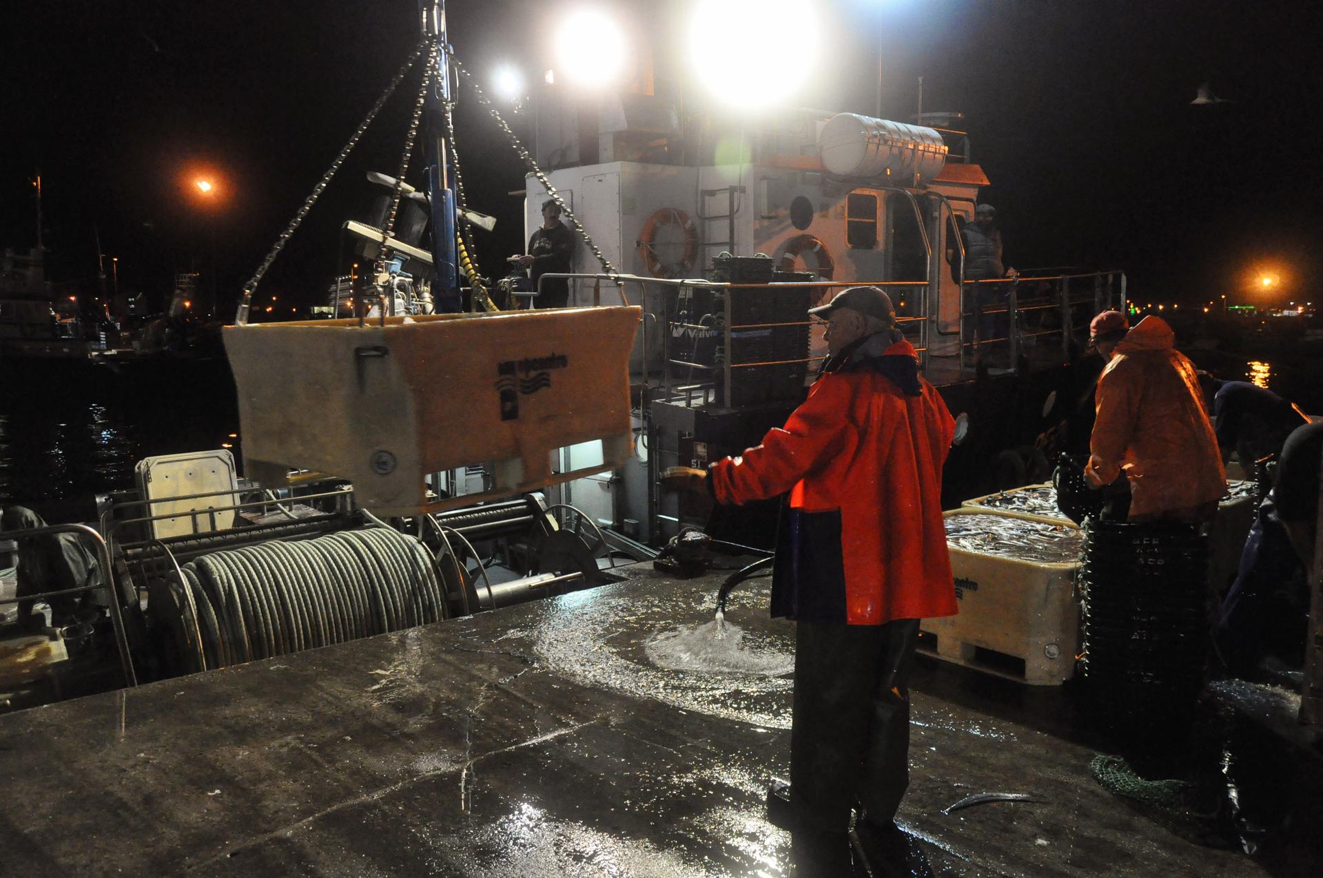 fishermen wait for a crain to lower a box of fish onto the docks