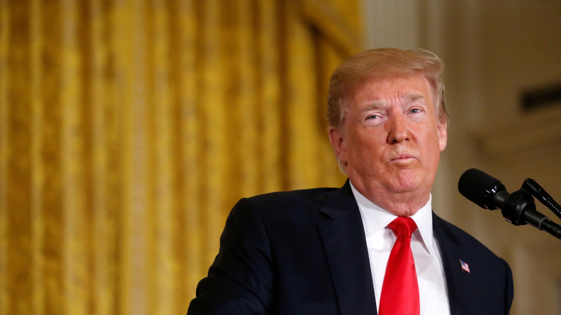 US President Donald Trump is seen looking to his right wearing a red tie and suit.