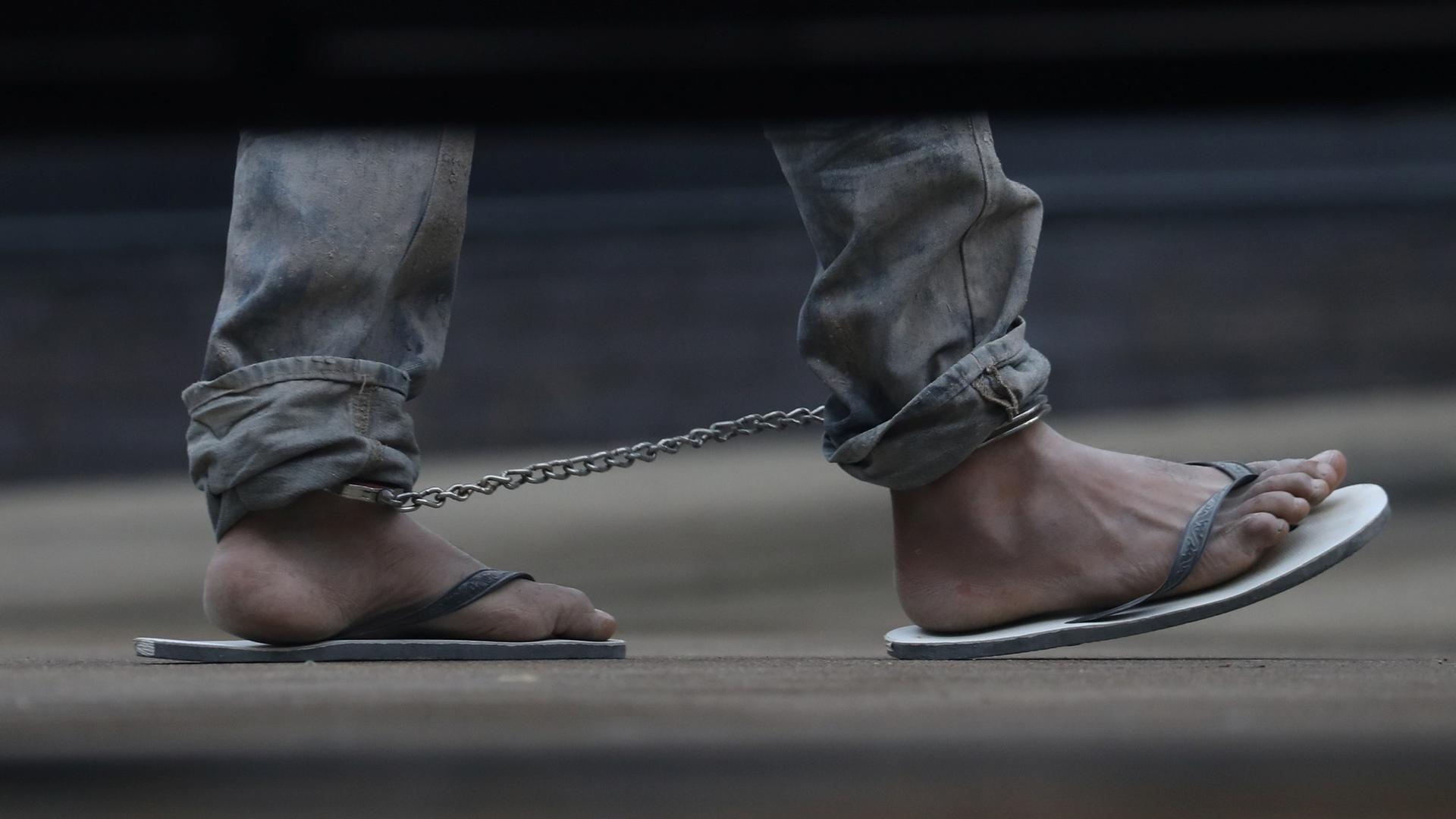 An undocumented immigrant is shown in shackles in a picture taken on the other side of a vehicle from underneath, just showing the feet.