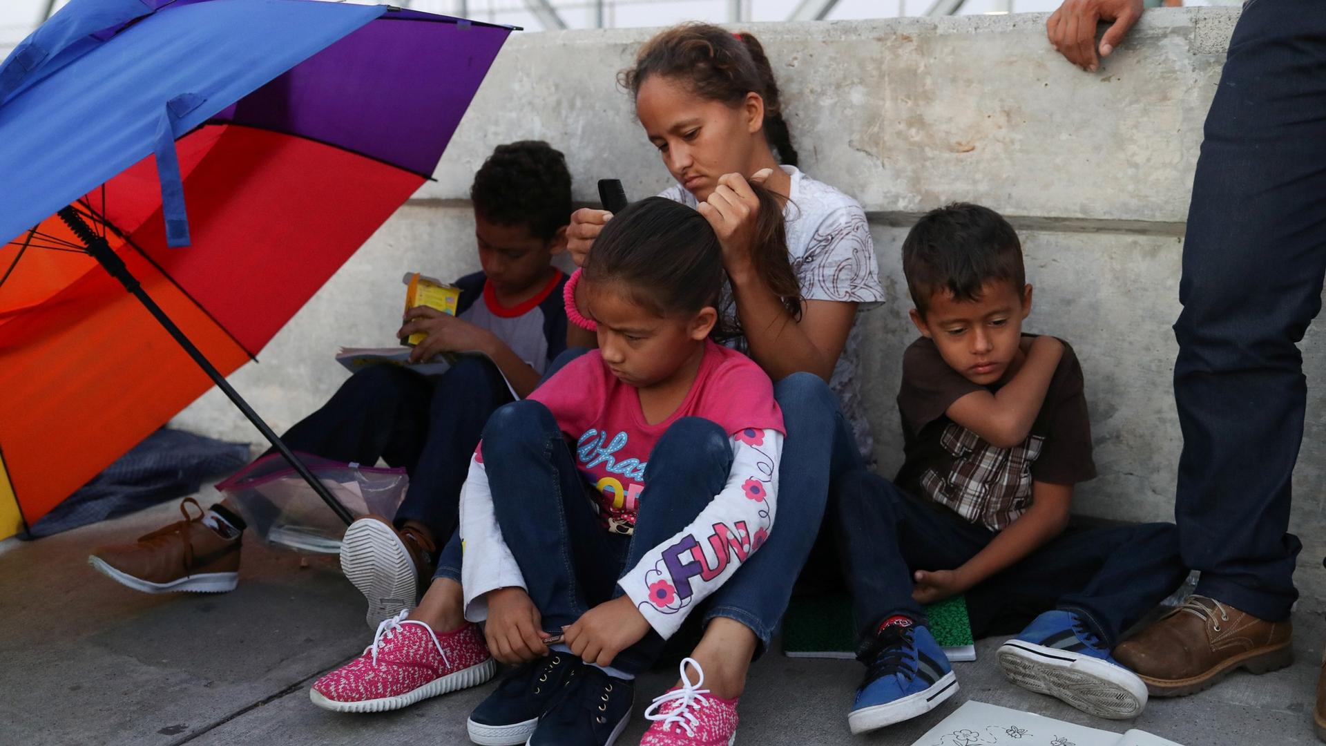 A Honduran family of three children and a mother seeking asylum sit with a colorful umbrella on the Mexican side of the Brownsville-Matamoros International Bridge.