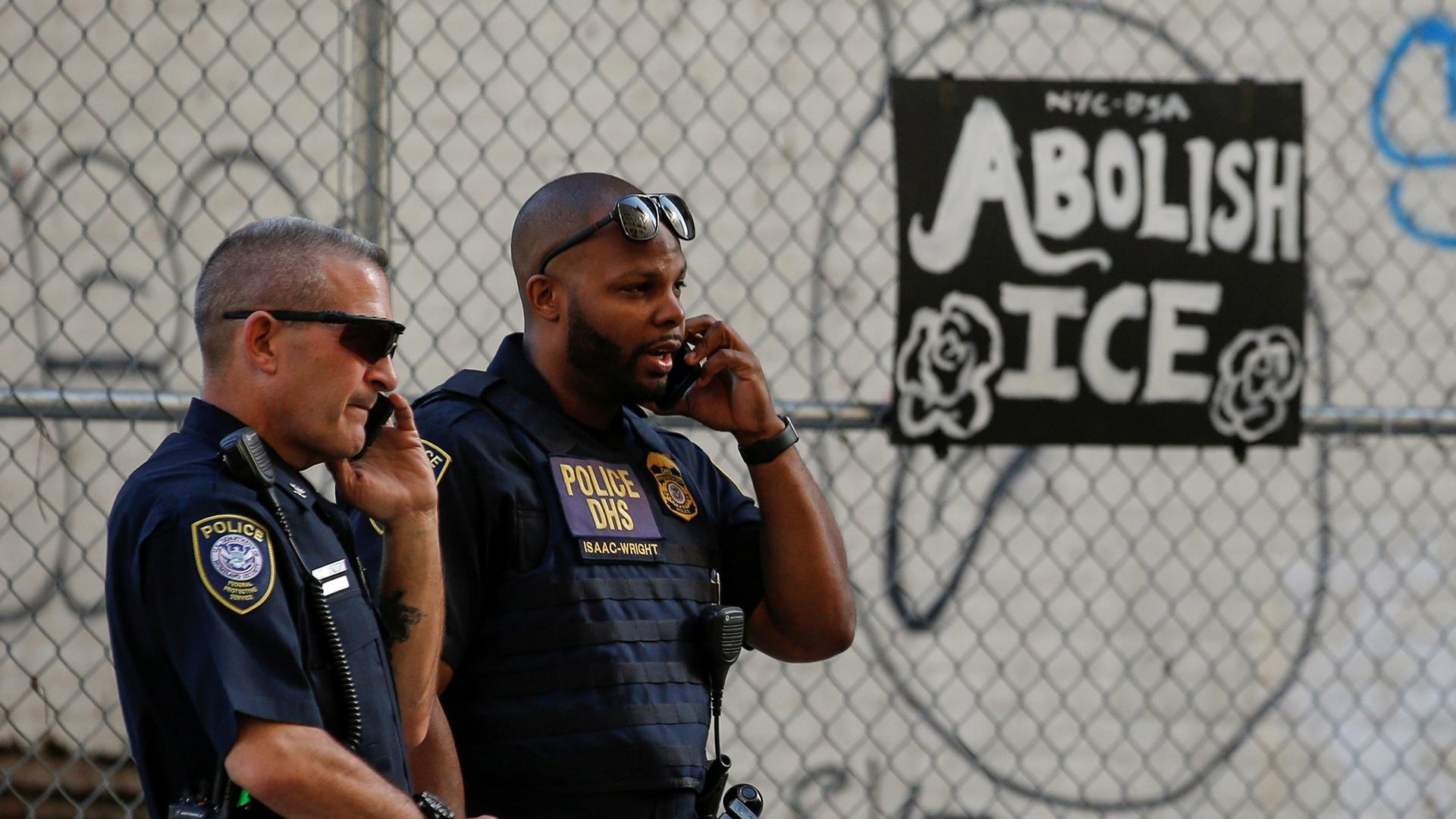 Two uniformed Department of Homeland Security officers are shown looking off to the right of the frame while talking on their walkie-talkies.