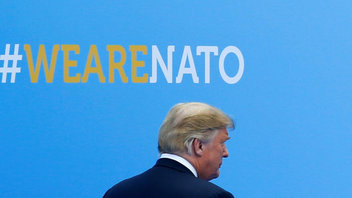 US President Donald Trump walks past a blue wall with #wearenato printed on it.