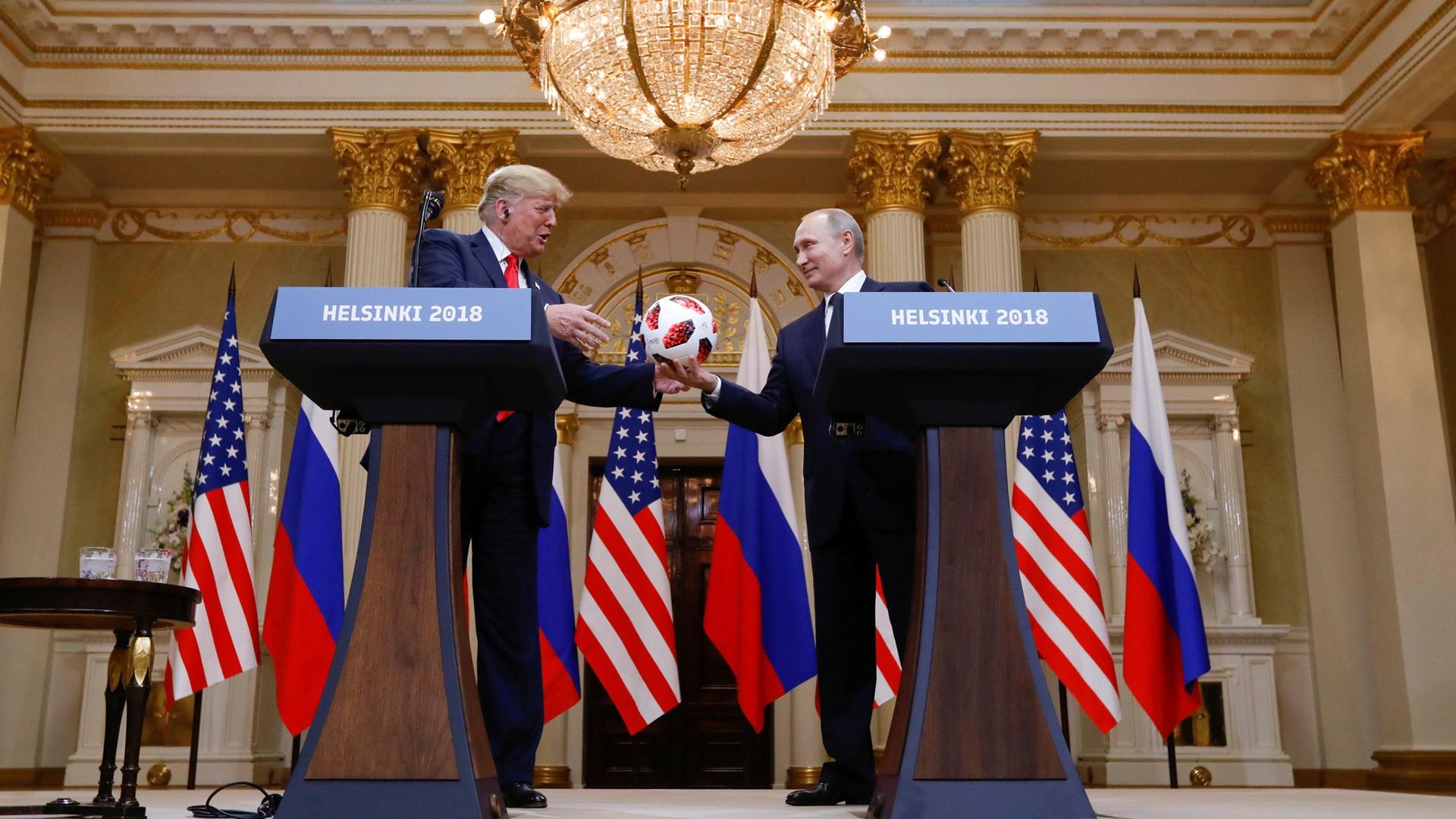 US President Donald Trump is handed a soccer ball from Russia's President Vladimir Putin while the two men stand behind podiums.