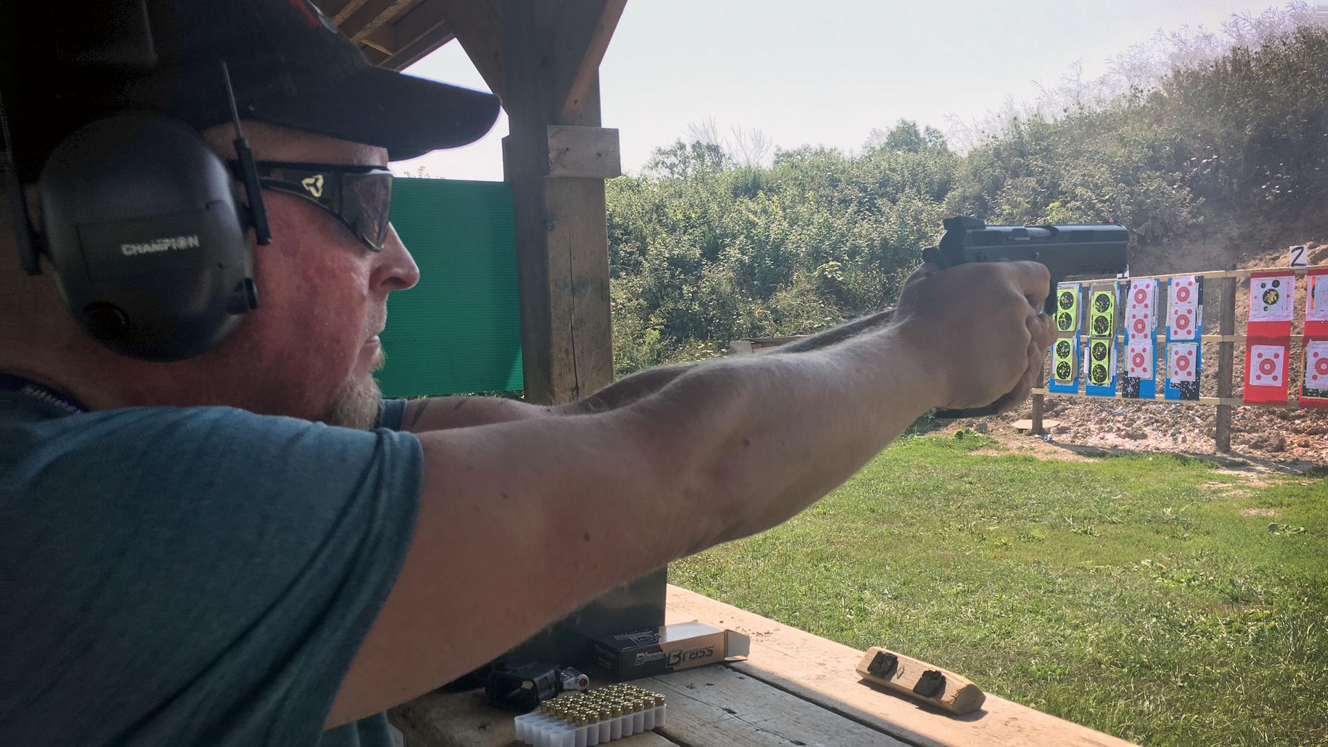 A man points a handgun at a target on a shooting range