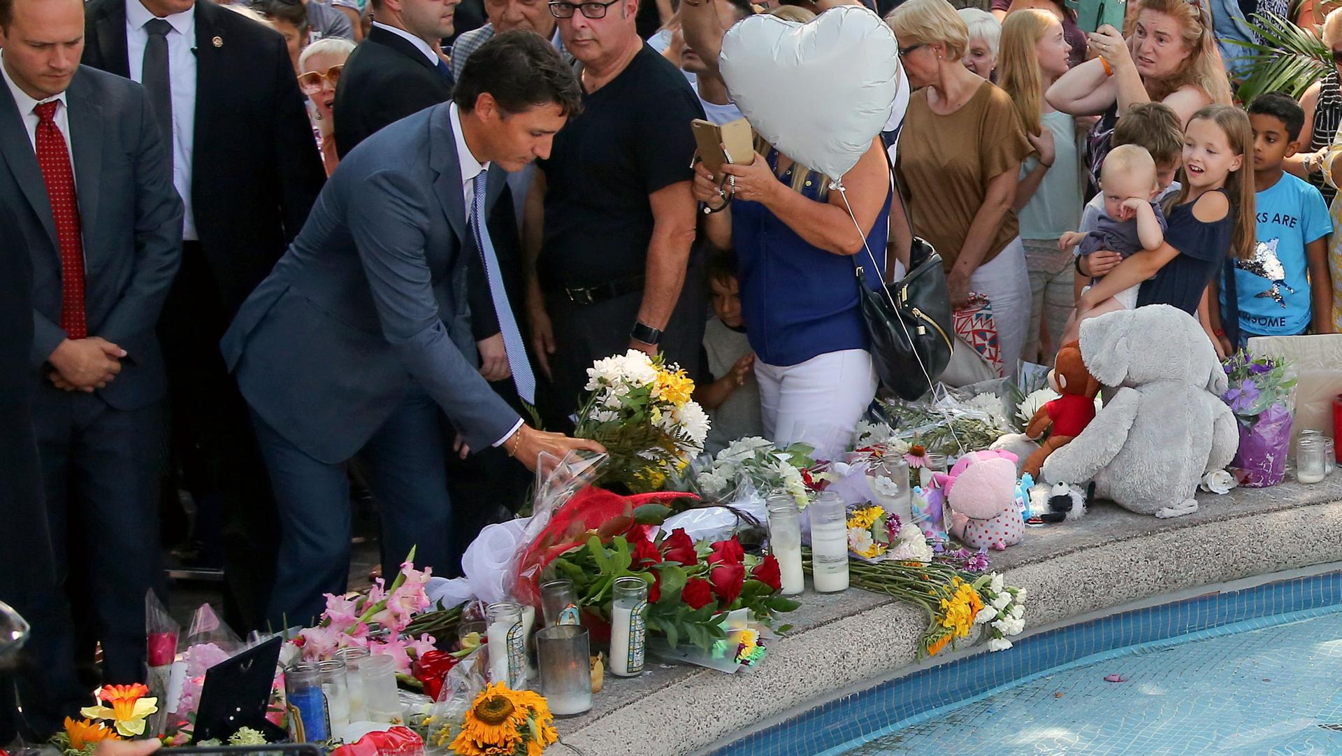 Canada's Prime Minister Justin Trudeau lays flowers at the site of a mass shooting. Around him is a large crowd assembled for a vigil.