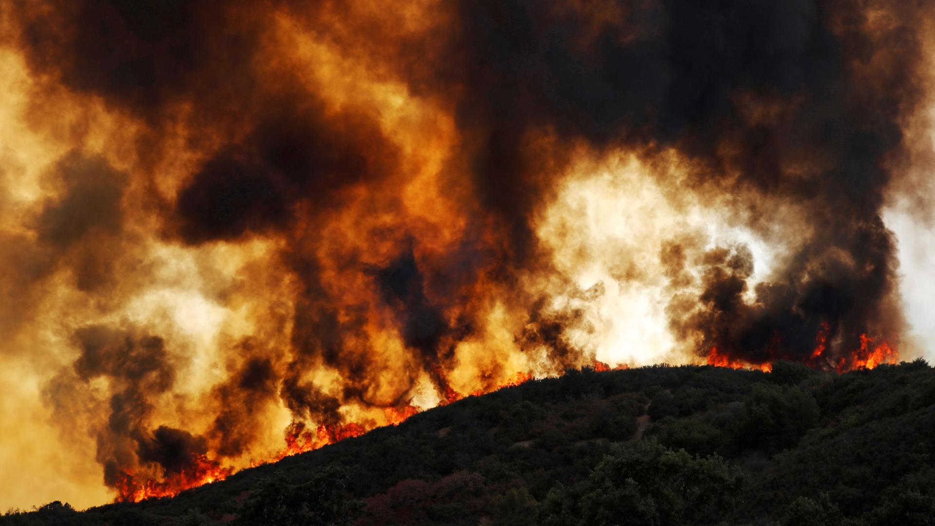 Wind-driven flames roll over a forested hill toward homes during near Lakeport, California, August 2, 2018.