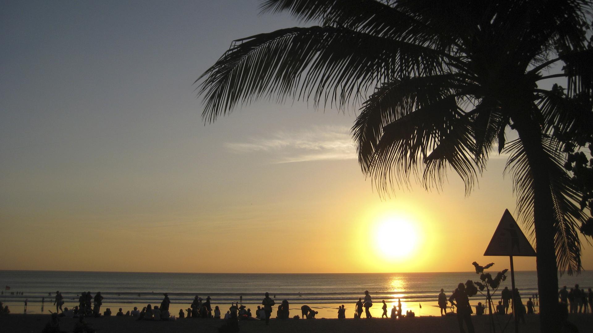 Beachgoers watch the sun set at Kuta beach in Bali, Indonesia