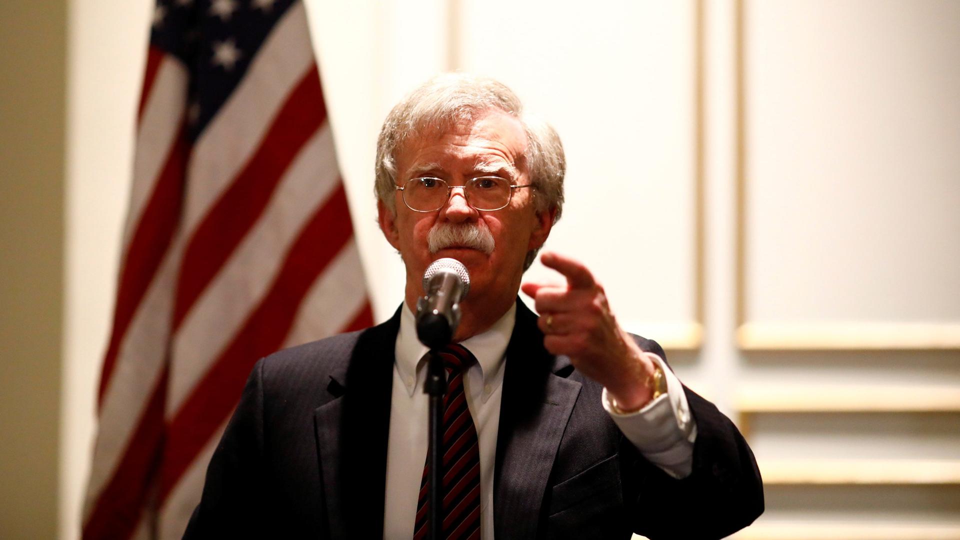 National Security Adviser John Bolton is shown at a microphone with the US flag behind him, speaking at a forum in Washington, DC, 2018.