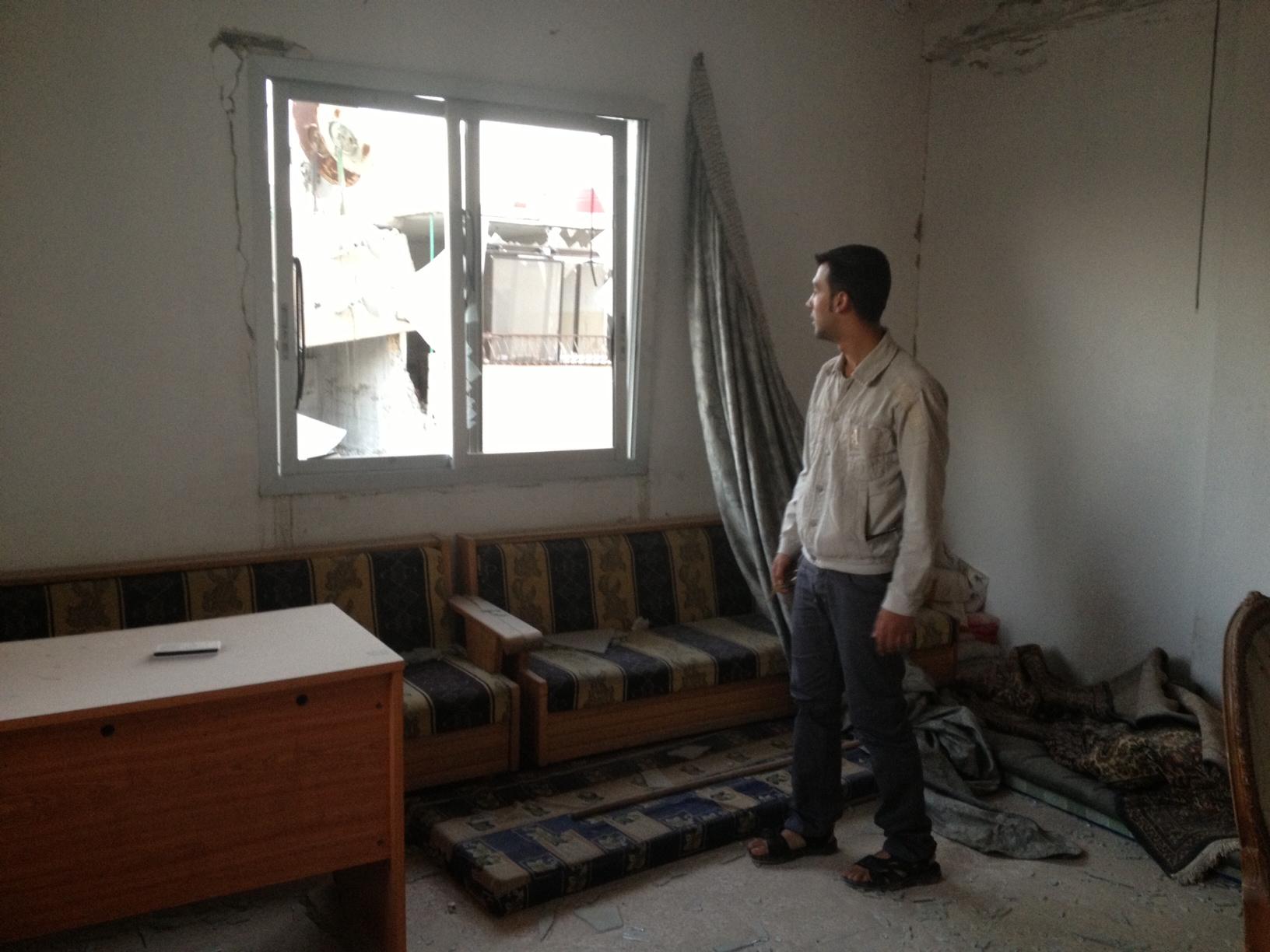 man looking out a broken window, surrounded by rubble