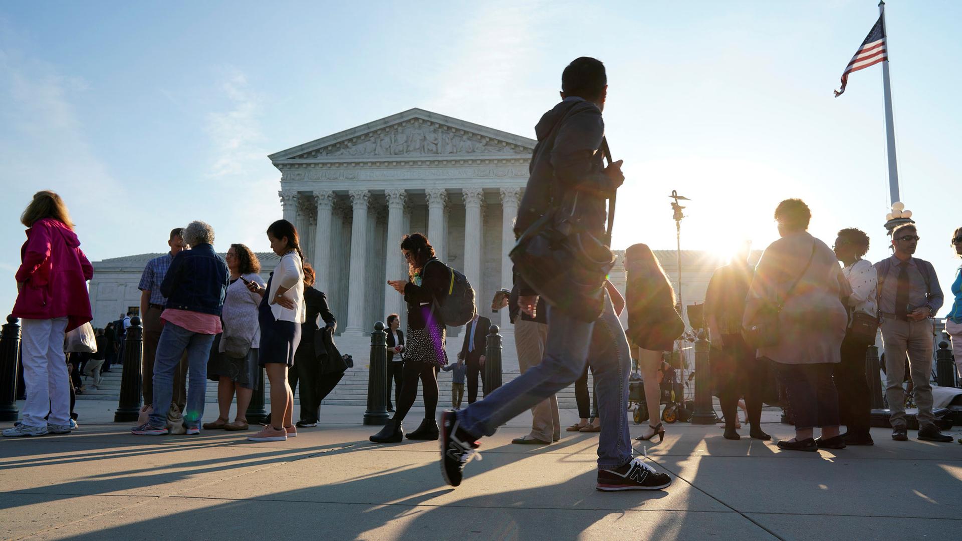 People are shown waiting in line with the Supreme Court in the background.