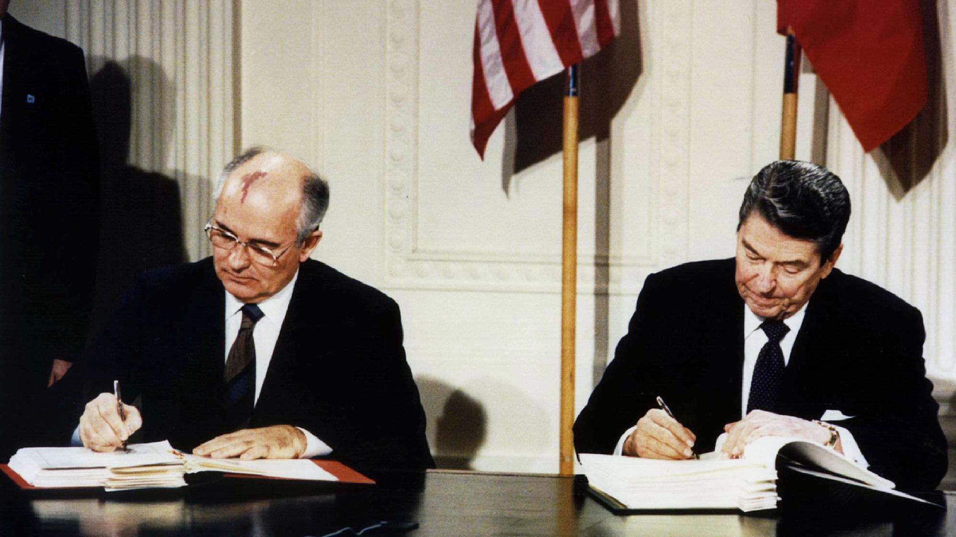 US President Ronald Reagan sits at a table to the left of Soviet President Mikhail Gorbachev while both men sign the Intermediate-Range Nuclear Forces treaty.