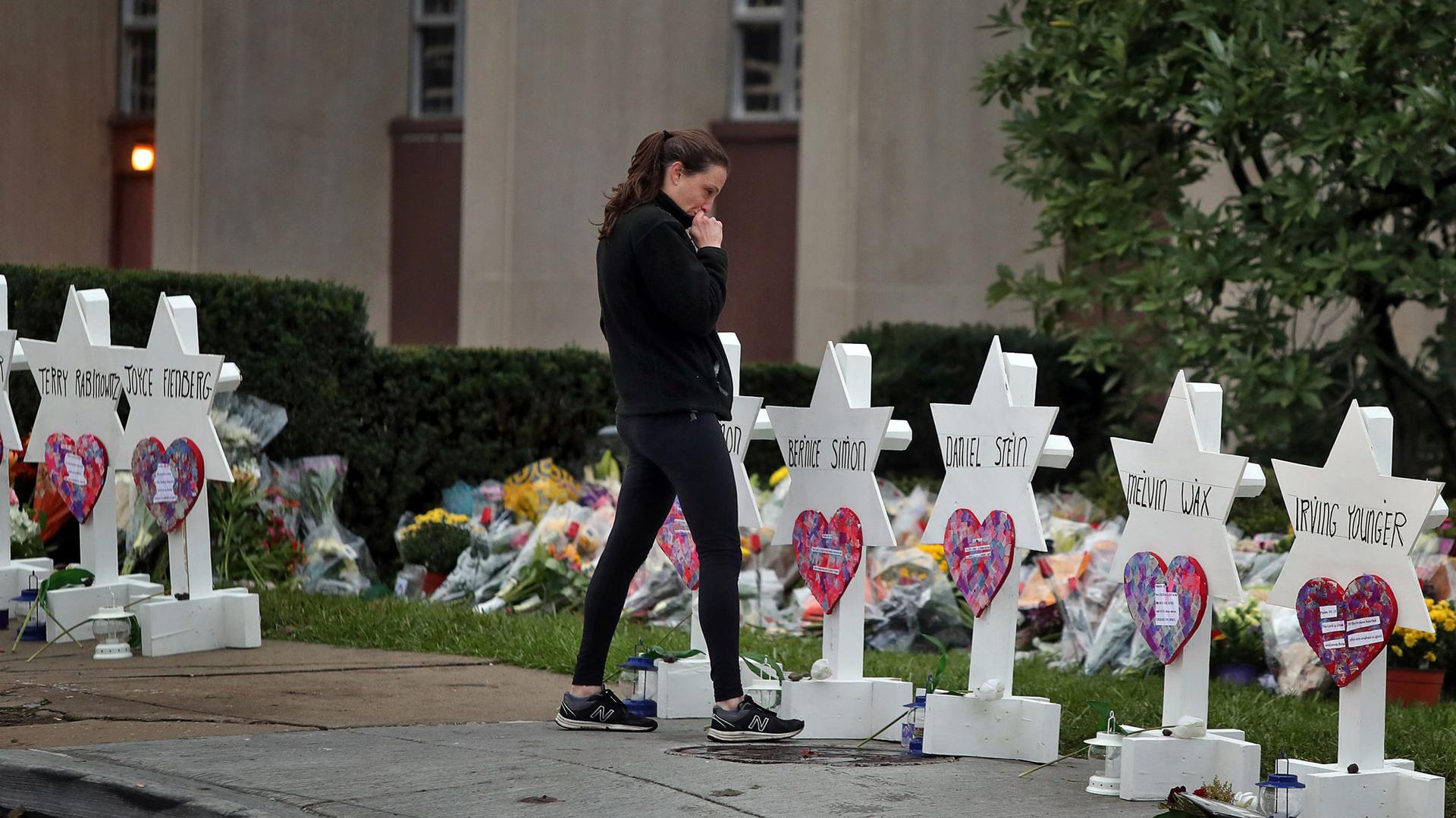 A woman is shown with her hand to her face standing at a makeshift memorial outside the Tree of Life synagogue.