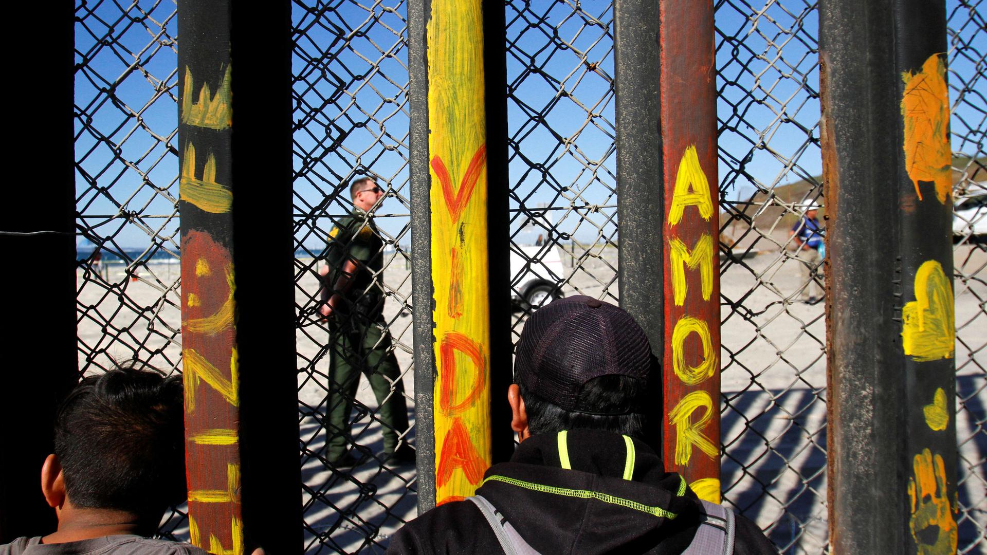 Migrants peer through a fence at a US soldier on the US side of the US-Mexico border.