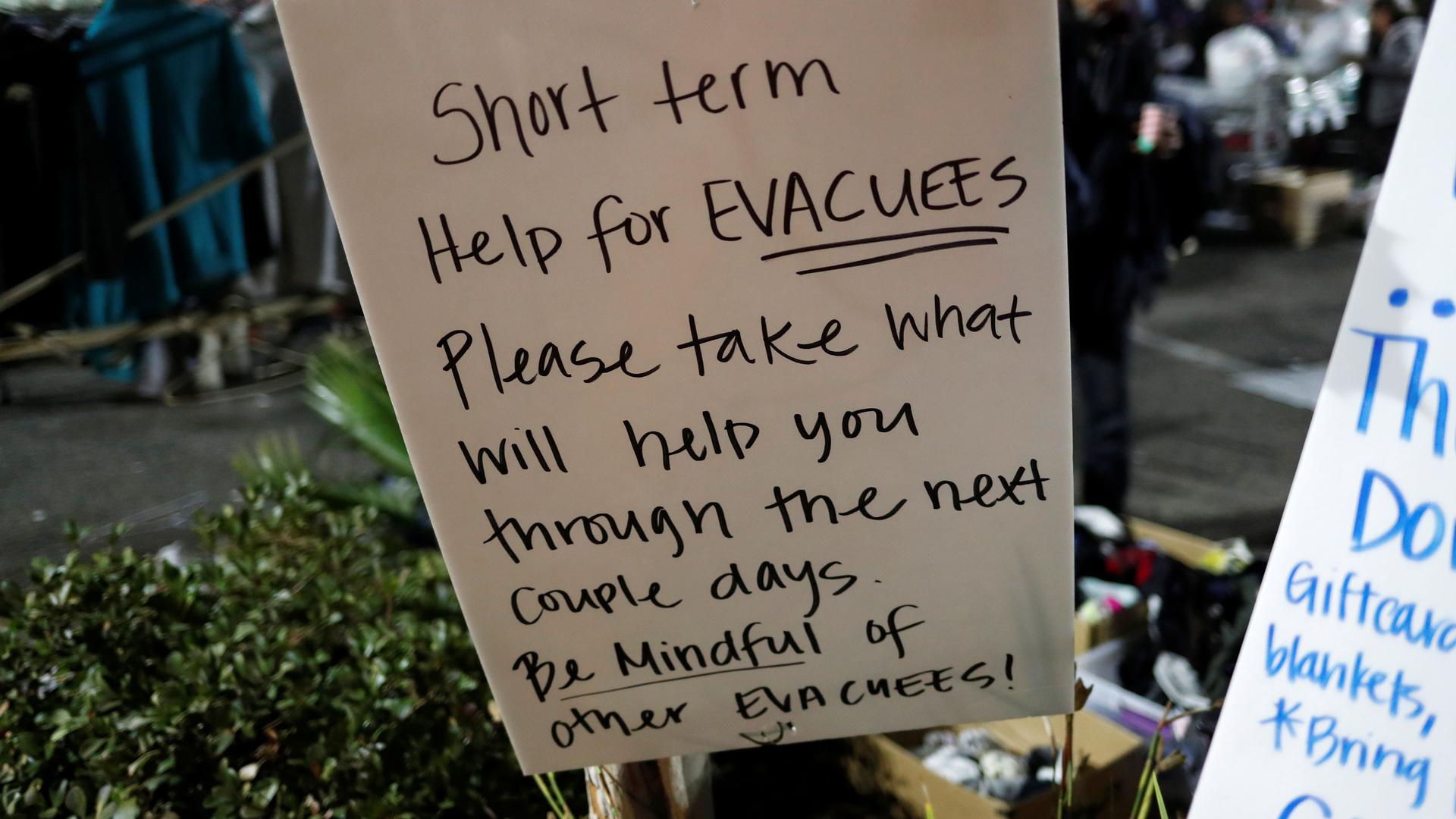 A handwritten sign says, "Short term help for evacuees. Please take what will help you through the next couple days. Be mindful of other evacuees!"