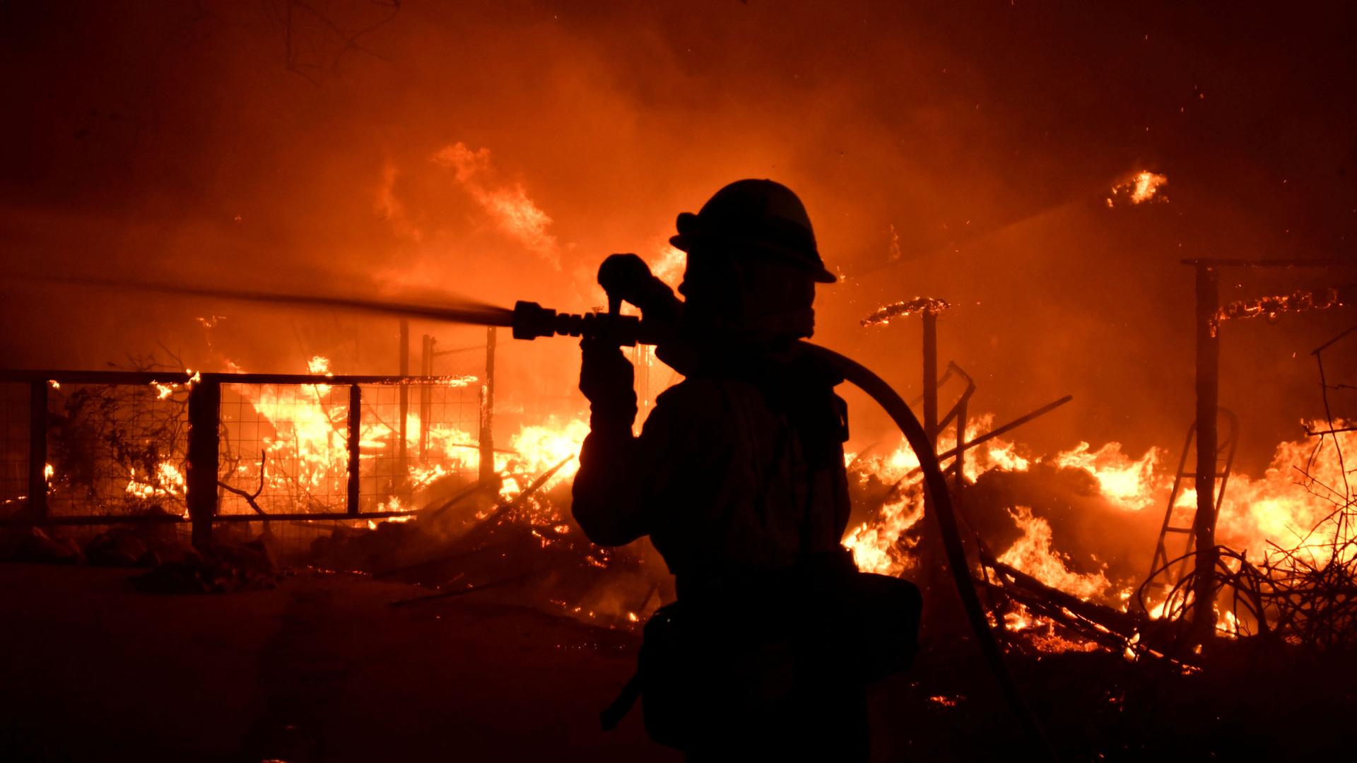 A firefighter is shown in silhouette with a hose over their shoulder and bright flames in the background.