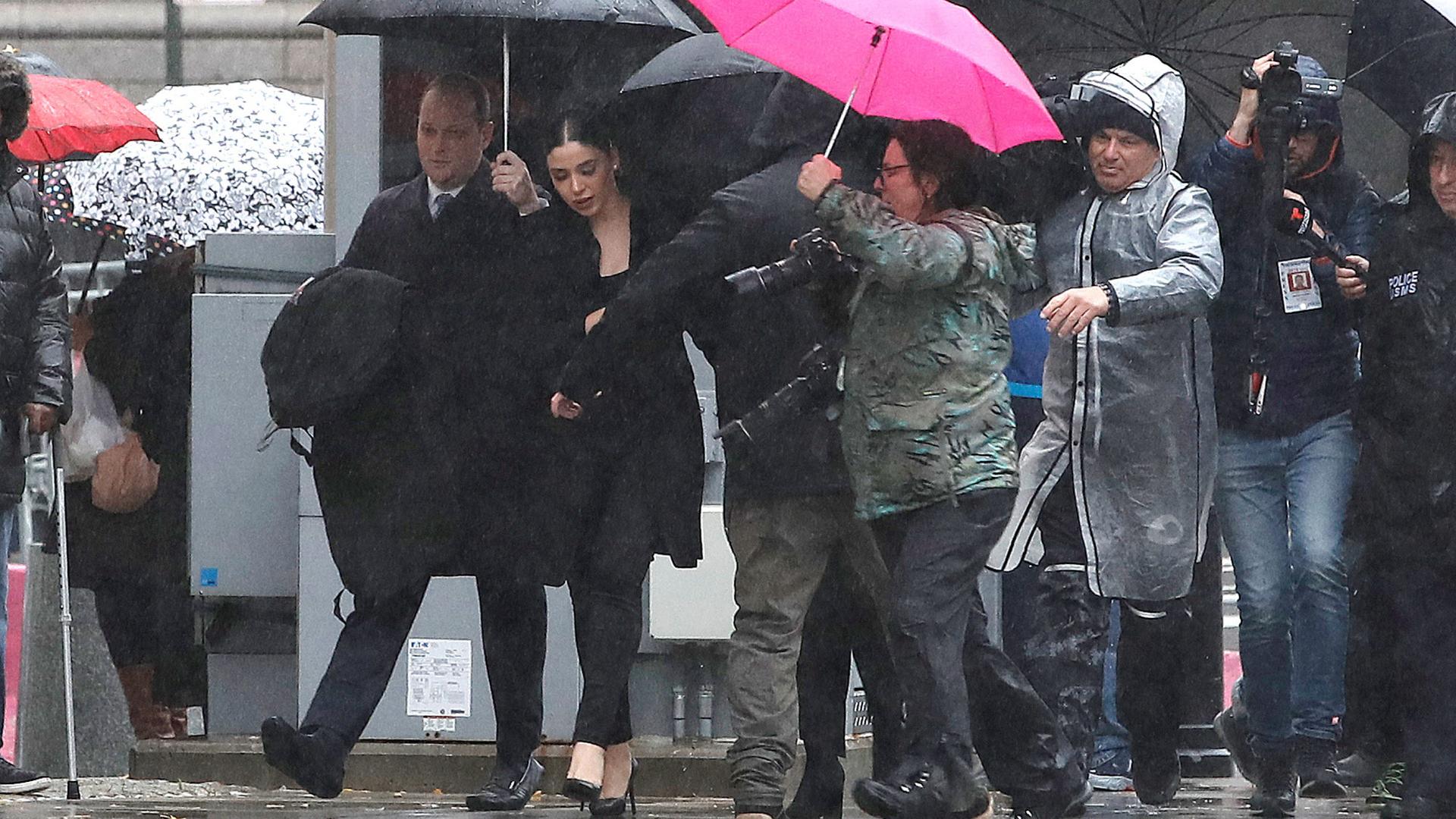 Emma Coronel Aispur is shown surrounded by several photographers walking while underneath umbrellas.