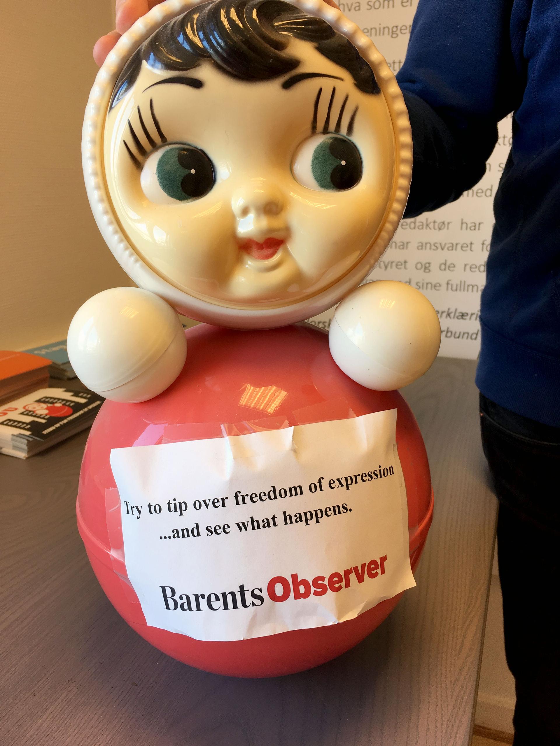 A large bobble-type doll has a paper sign that reads, 