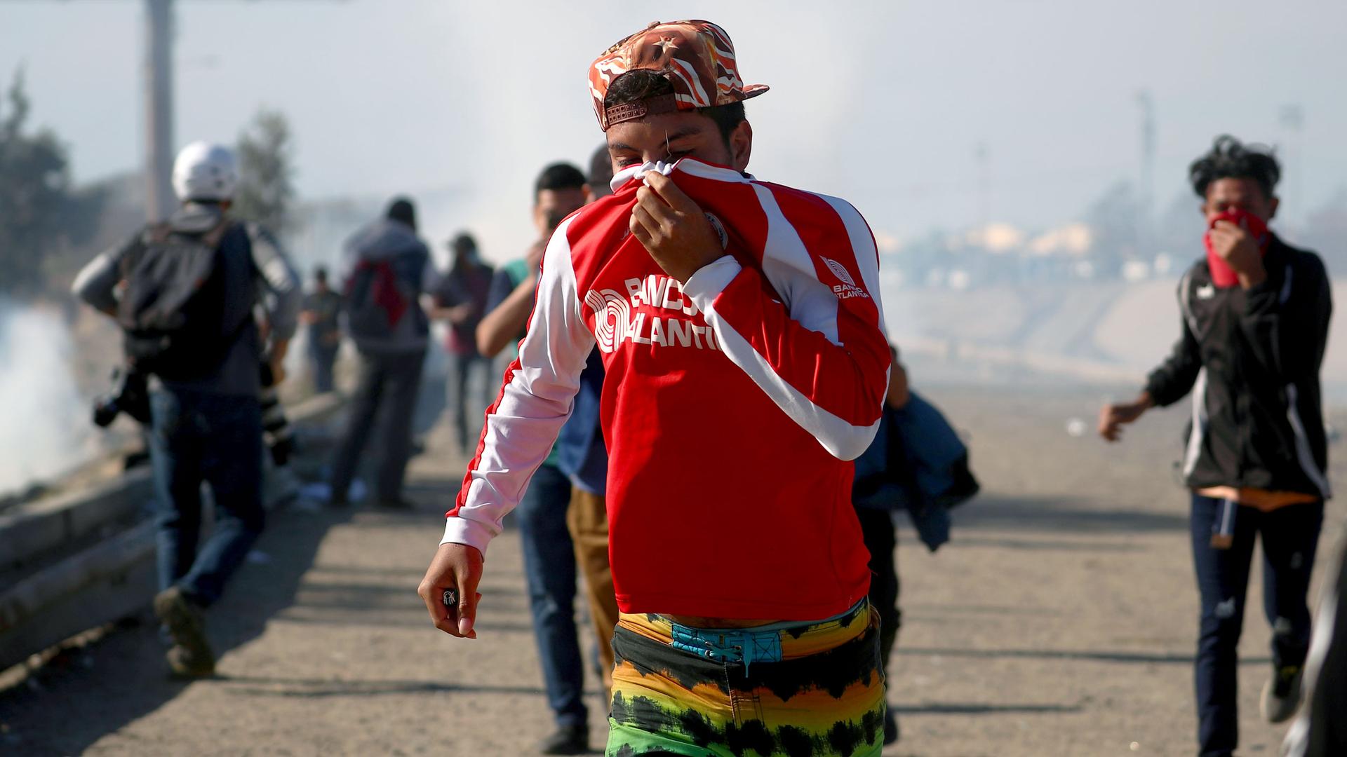 A man uses his shirt to cover his face as he runs from tear gas