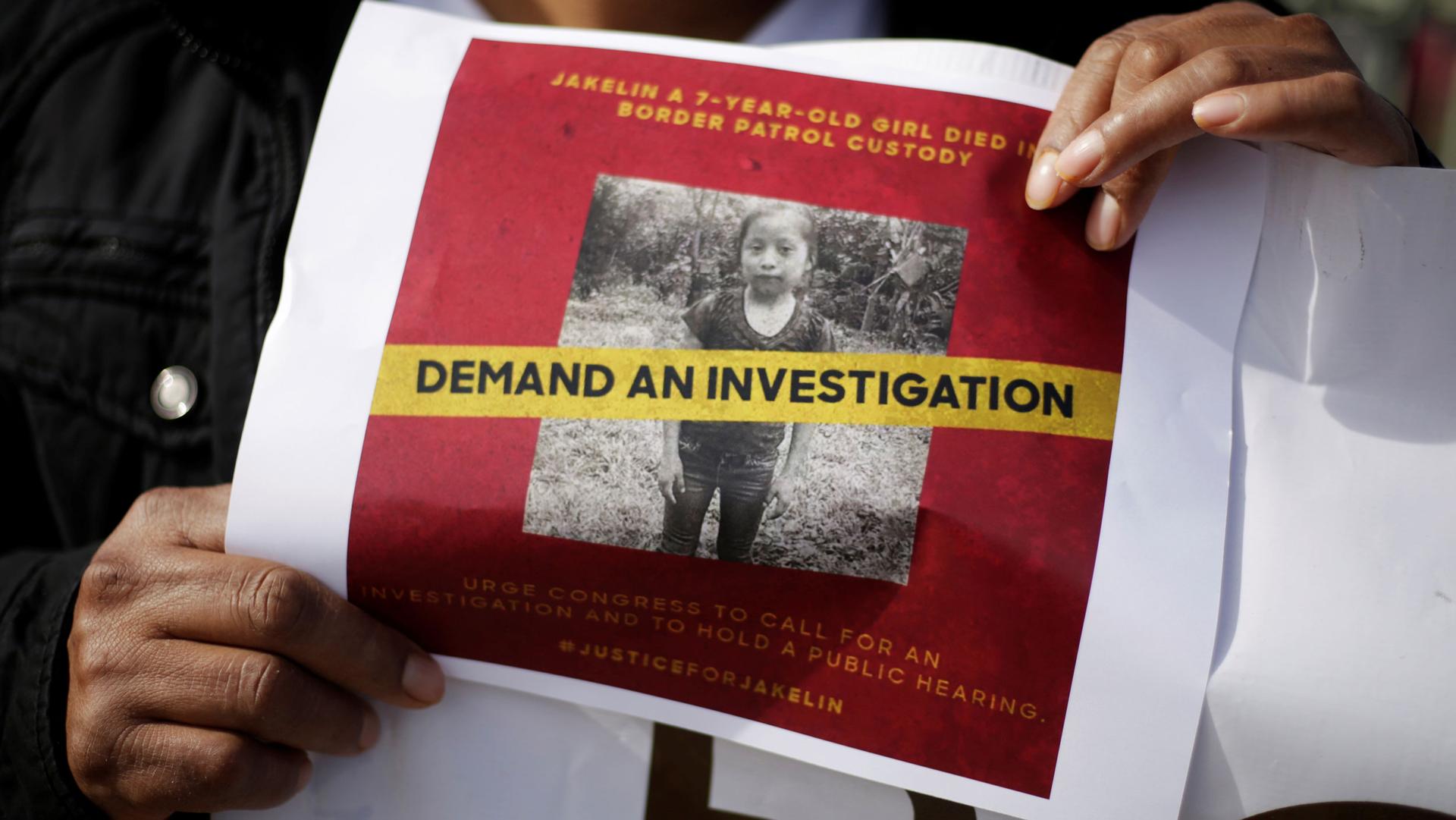 Two hands hold up a piece of paper with a red background that reads "Demand an investigation"