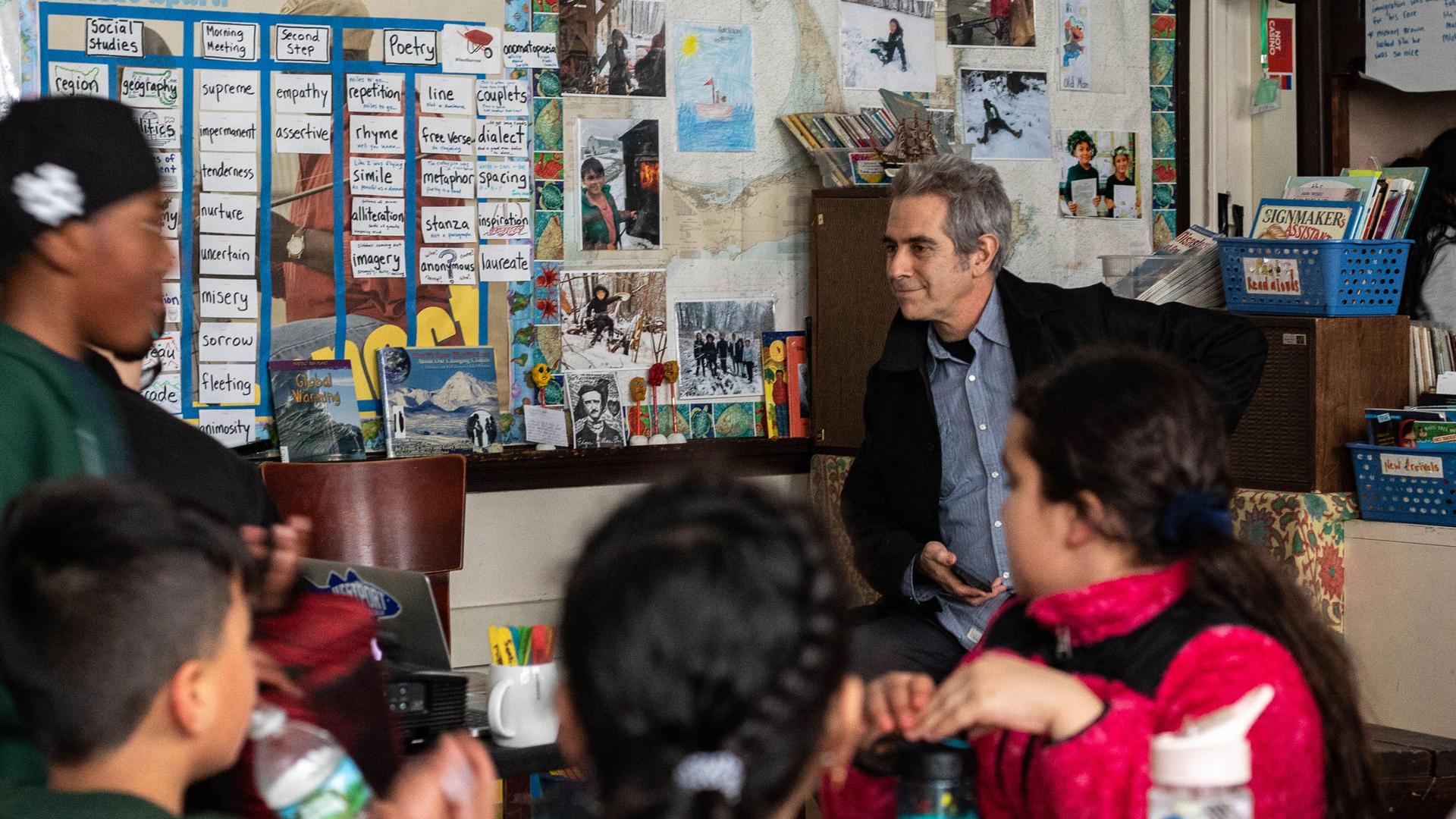 Host Marco Werman looks on as children from a fourth grade class in East Boston discuss a poem written on a white board.