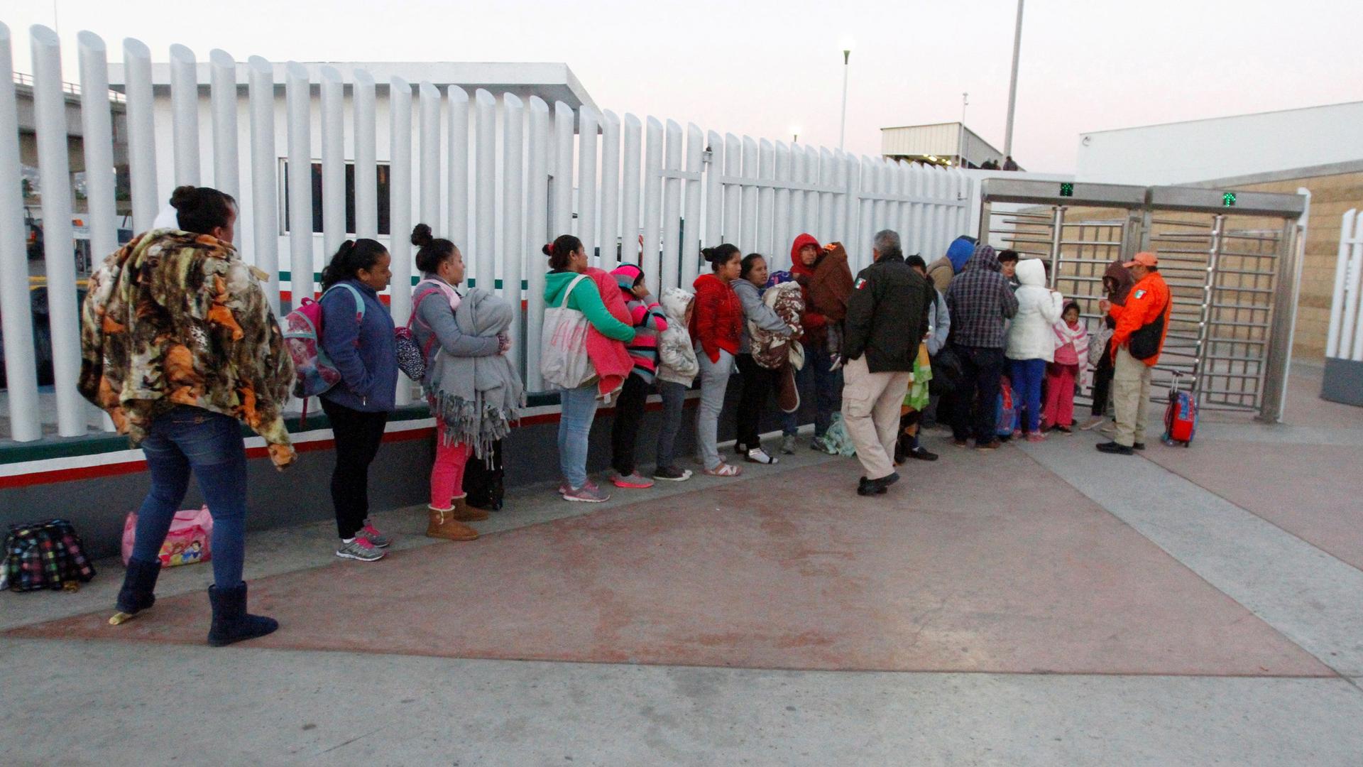 People stand in a line against a tall metal wall