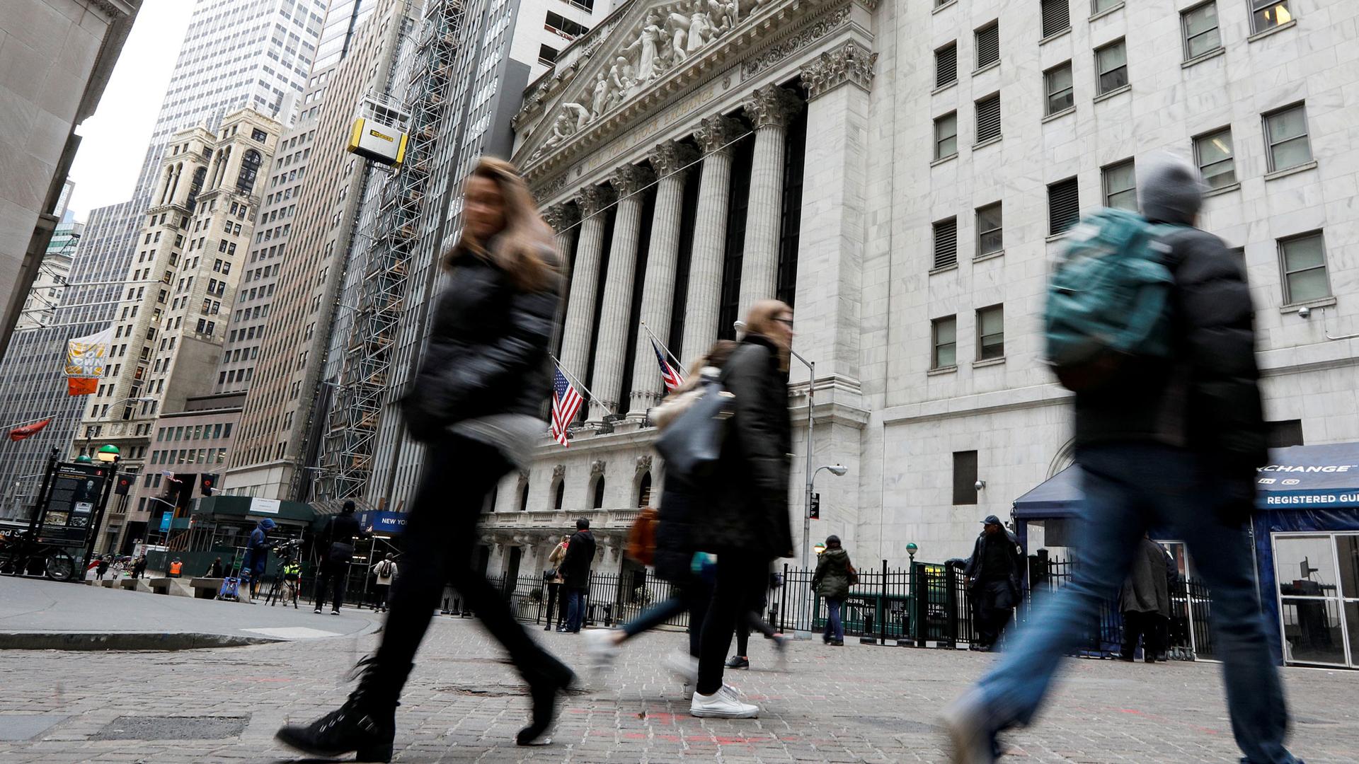 People are shown in blurred motion walking in front of the New York Stock Exchange.